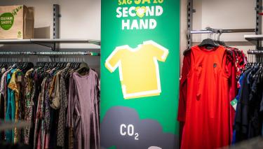Stilvoll, günstig und nachhaltig: Secondhand ist eine bewusste Konsumentscheidung, die sich einfach besser anfühlt. Im Oxfam Shop Berlin-Weißensee hängt Kleidung in bunten Farben auf Kleiderständern. Dazwischen hängt ein Schild mit der Aufschrift „Sag ja zu Second Hand“.