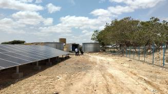 Solarbetriebene Entsalzungsanlage in Ceel Afwayn, Somalia. Solarpaneele und ein großer Wassertank. Sehr weit hinten im Bild unterhalten sich mehrere Menschen.