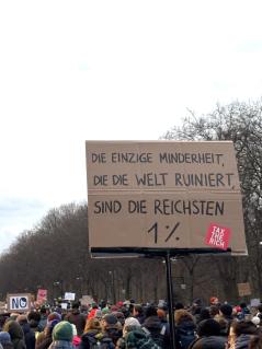 "Die einzige Minderheit, die die Welt ruiniert, sind die reichsten 1 %" viele Menschen mit Demoschildern bewegen sich auf den Großen Stern in Berlin zu. Auf einem Schild steht "Die einzige Minderheit, die die Welt ruiniert, sind die reichsten 1 %"