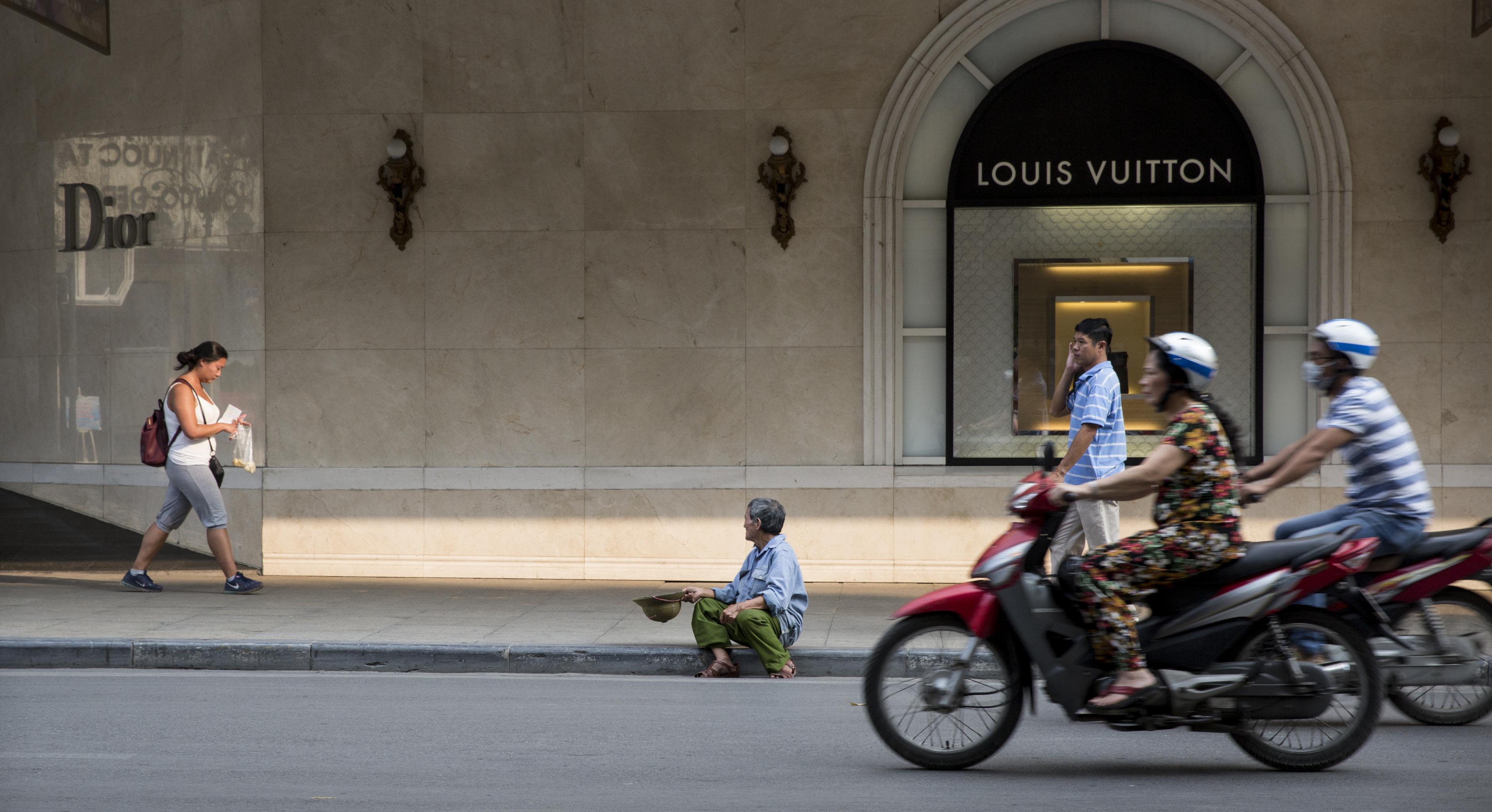 Mann sitzt vor Louis-Vuitton-Laden in Hanoi und bettelt