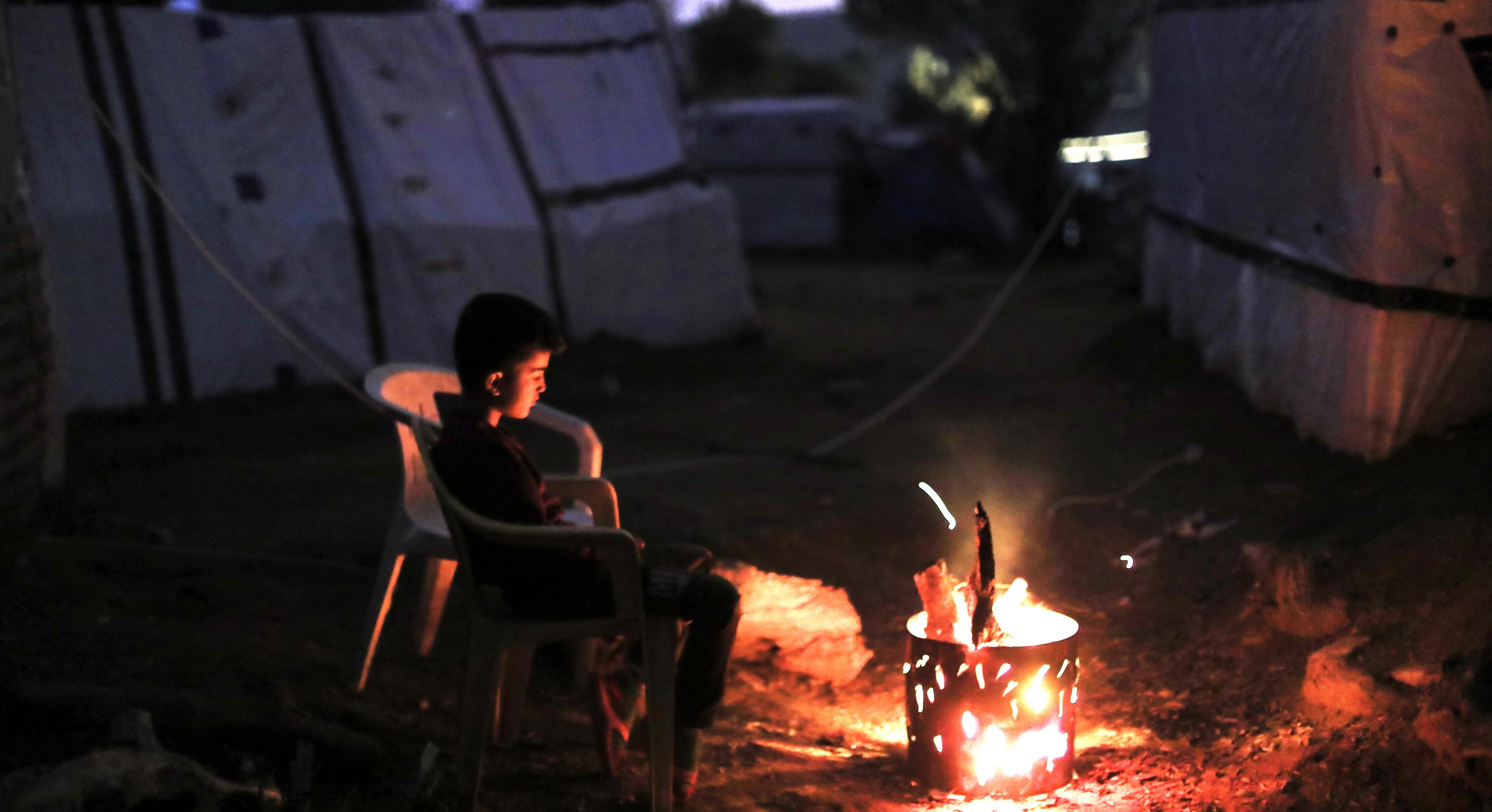 Ein Junge sitzt in einem Flüchtlingscamp vor einem kleinen Feuer
