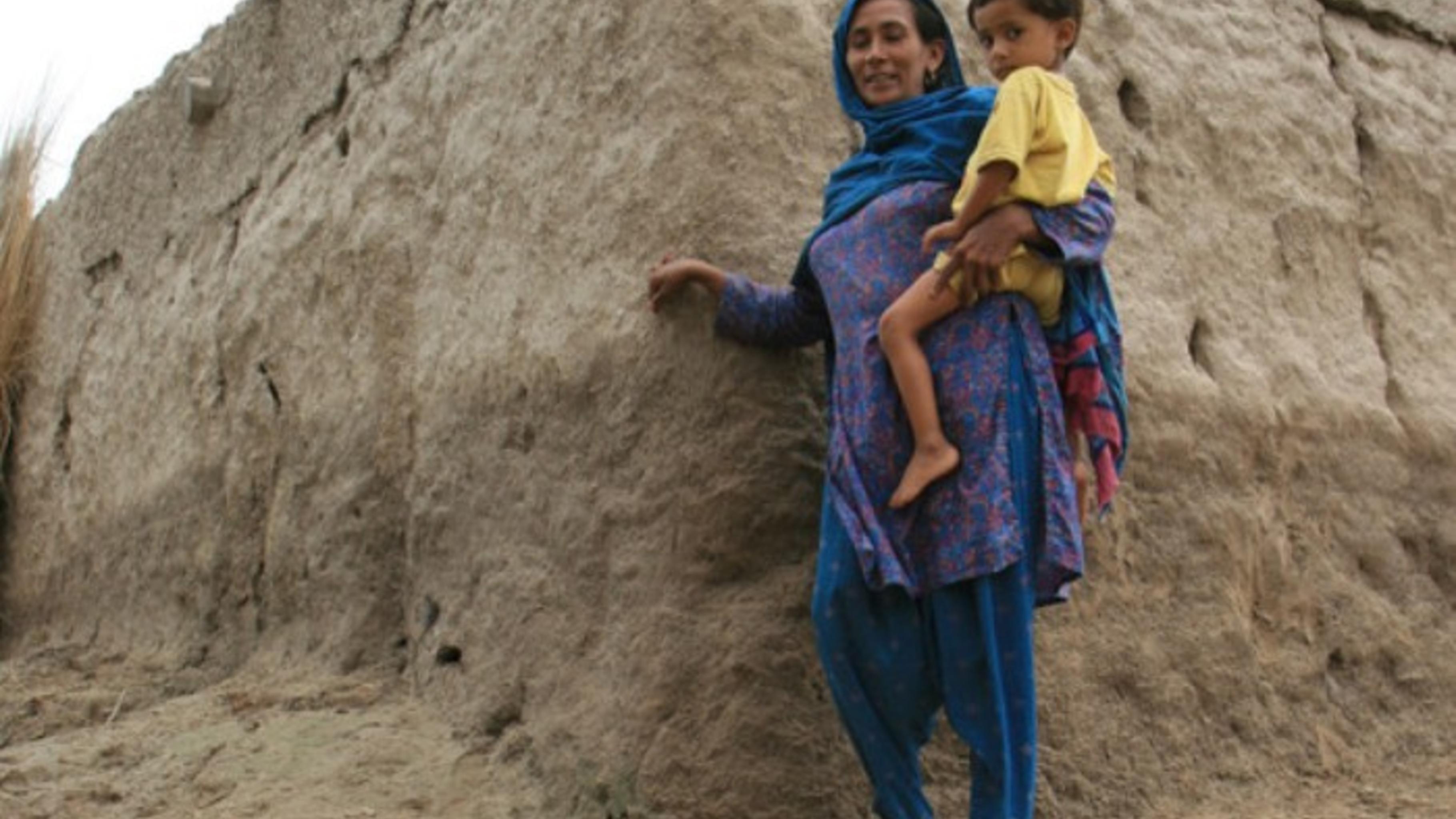 Syeda, mit ihrem Sohn Mohsin (3) auf dem Arm, zeigt den Wasserstand an ihrer kle