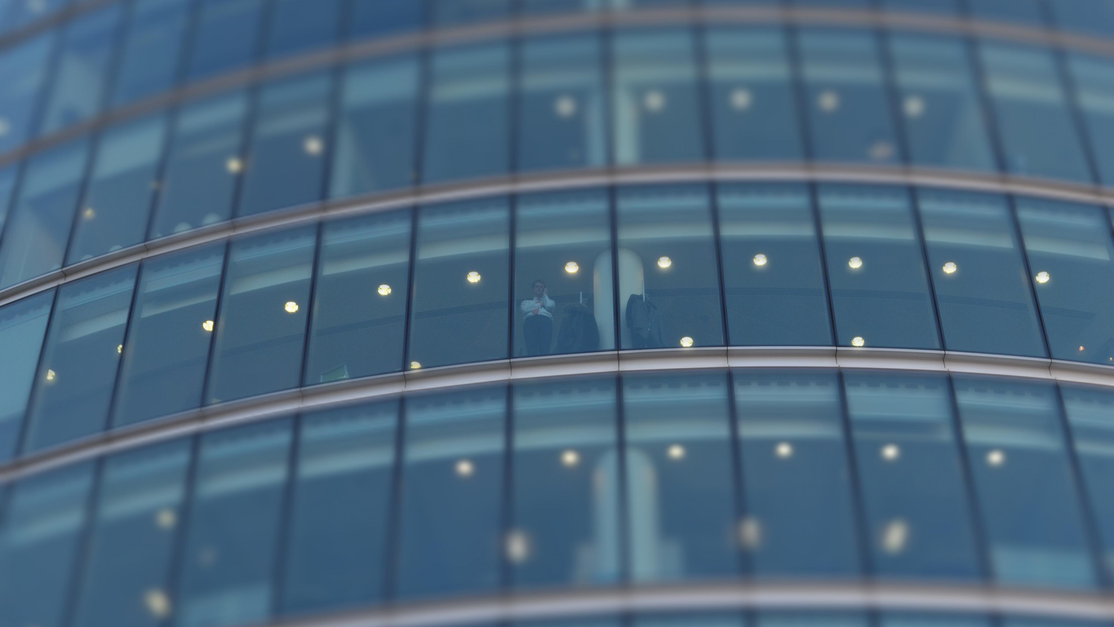 Ein Mann telefoniert in einem hohen Gebäude mit Fensterfront.