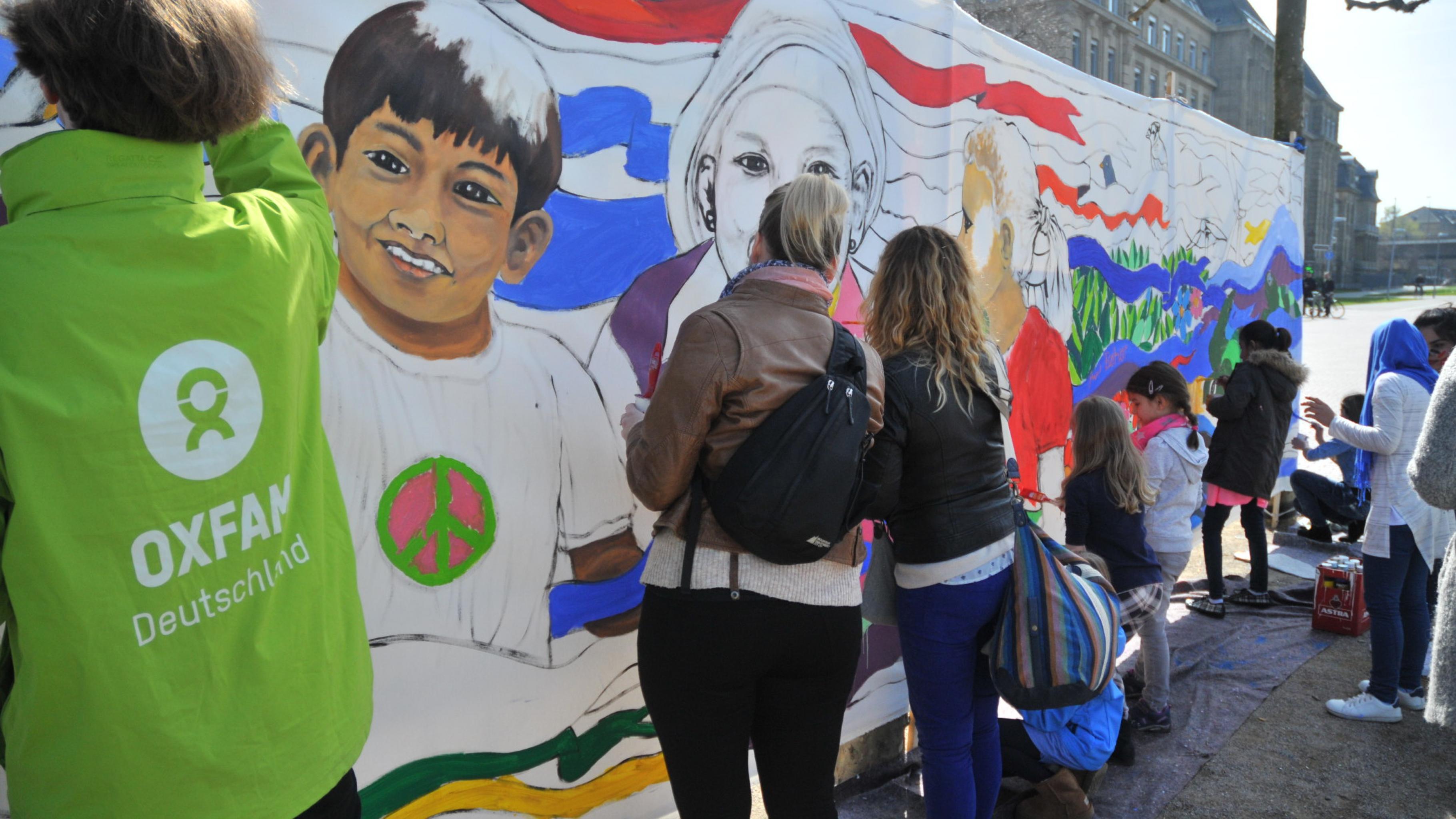 Kinder und Erwachsene malen auf einer 8x2 Meter großen Leinwand an einem halb fertigen Bild.