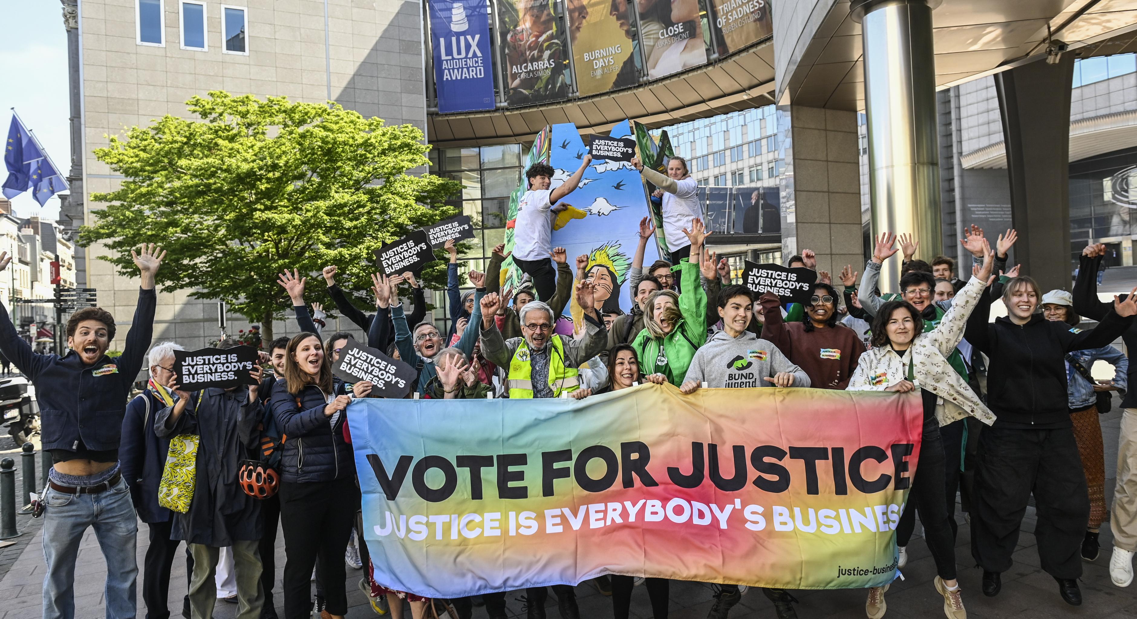 Eine Gruppe von etwa 30 Menschen hält vor dem Brüsseler Gebäude des EU-Parlaments ein Banner mit der Aufschrift „Vote for Justice – Justice is Everybody's Business“ und freut sich einen Keks.