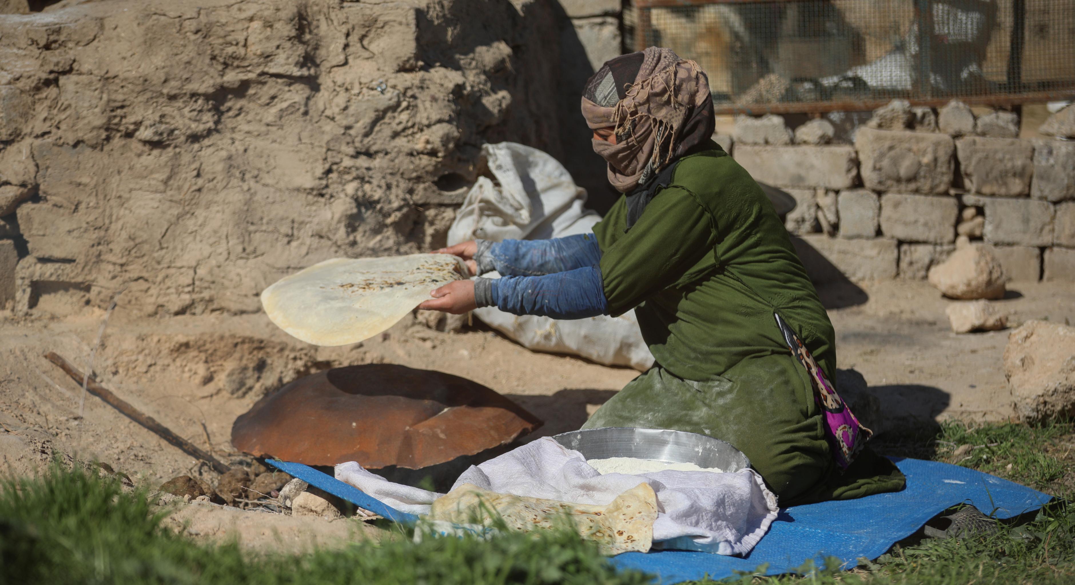 Eine Frau kniet auf dem Boden und nimmt ein Fladenbrot von einem kleinen Ofen. Sie befindet sich in Deir ez-Zor in Syrien.