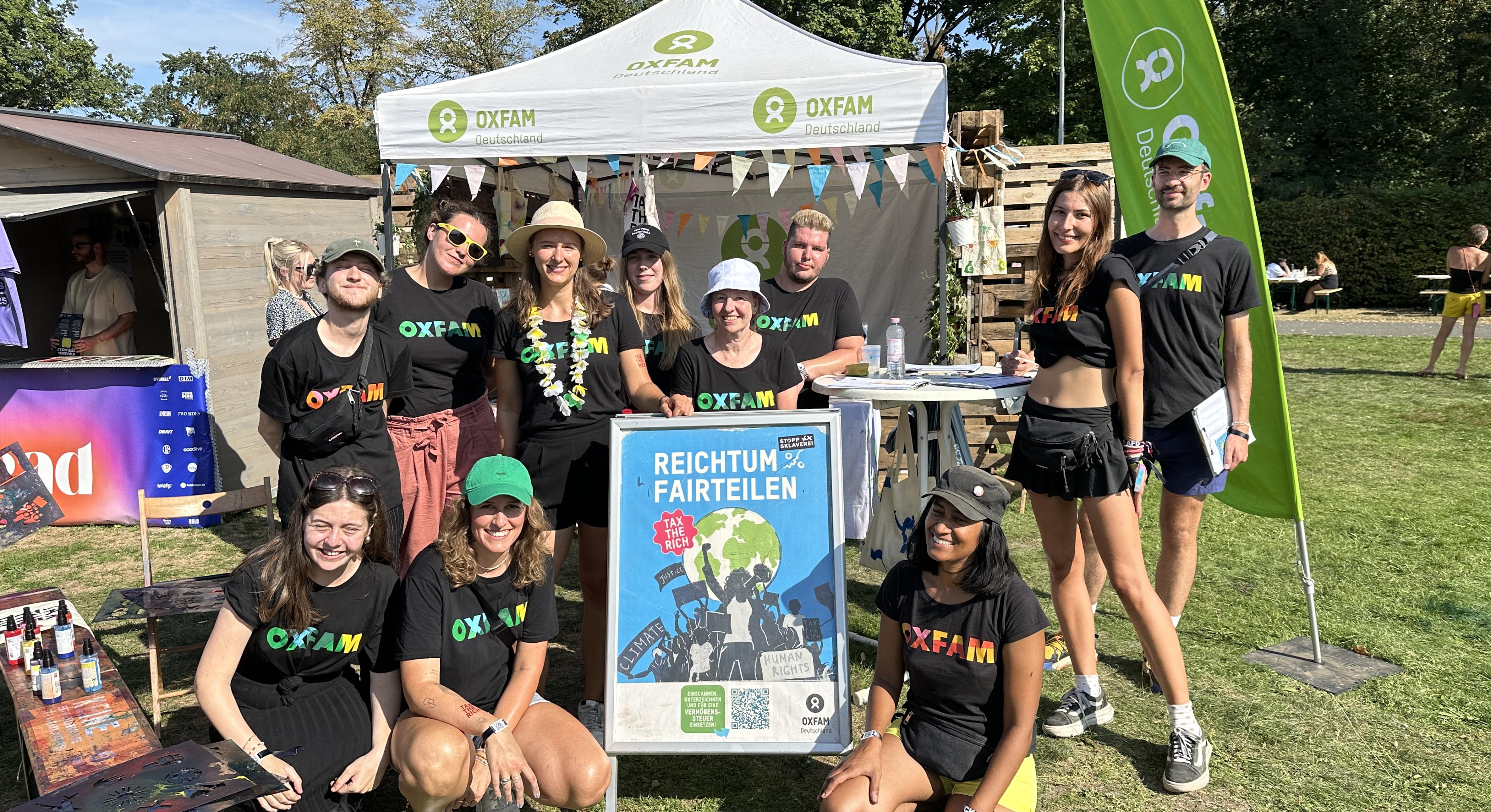 Eine Gruppe von Menschen steht vor einem Festivalstand von Oxfam