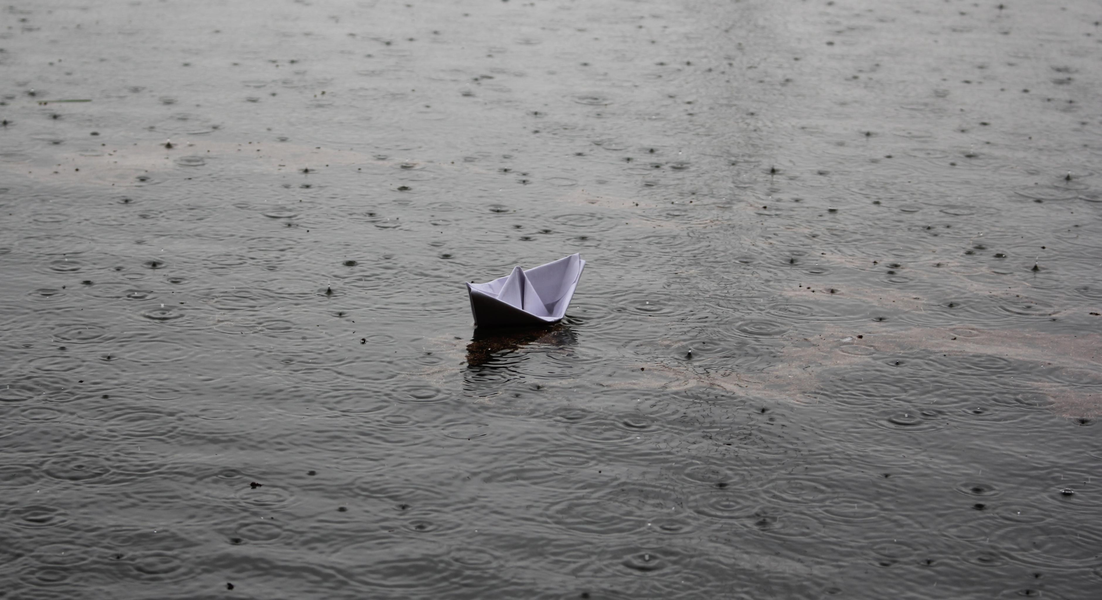 Regen prasselt auf ein schwimmendes Papierboot