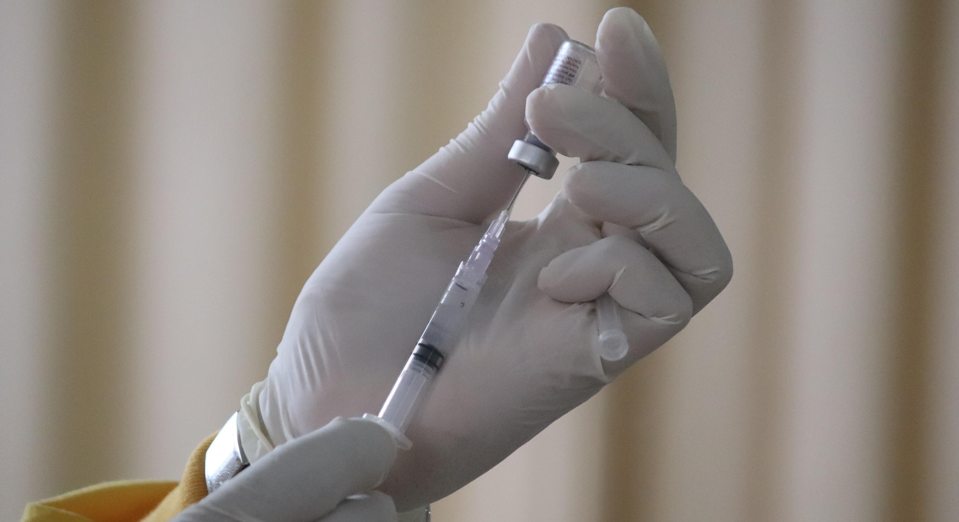 Nahaufnahme von Händen in Handschuhen beim Aufziehen einer Impfdosis
