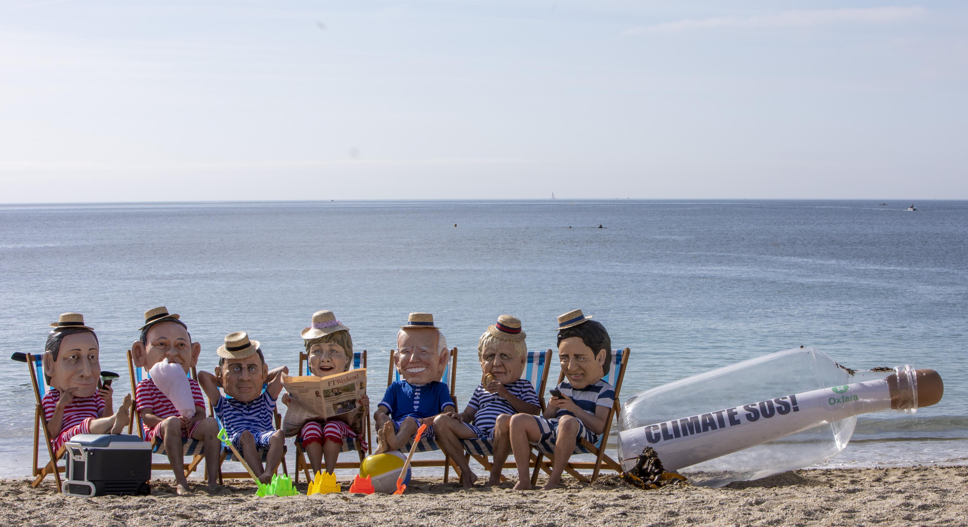 Aktivist*innen posieren als G7-Regierungschef*innen am Strand. Sie tragen gestreifte Badesachen und Sonnenhüte.
