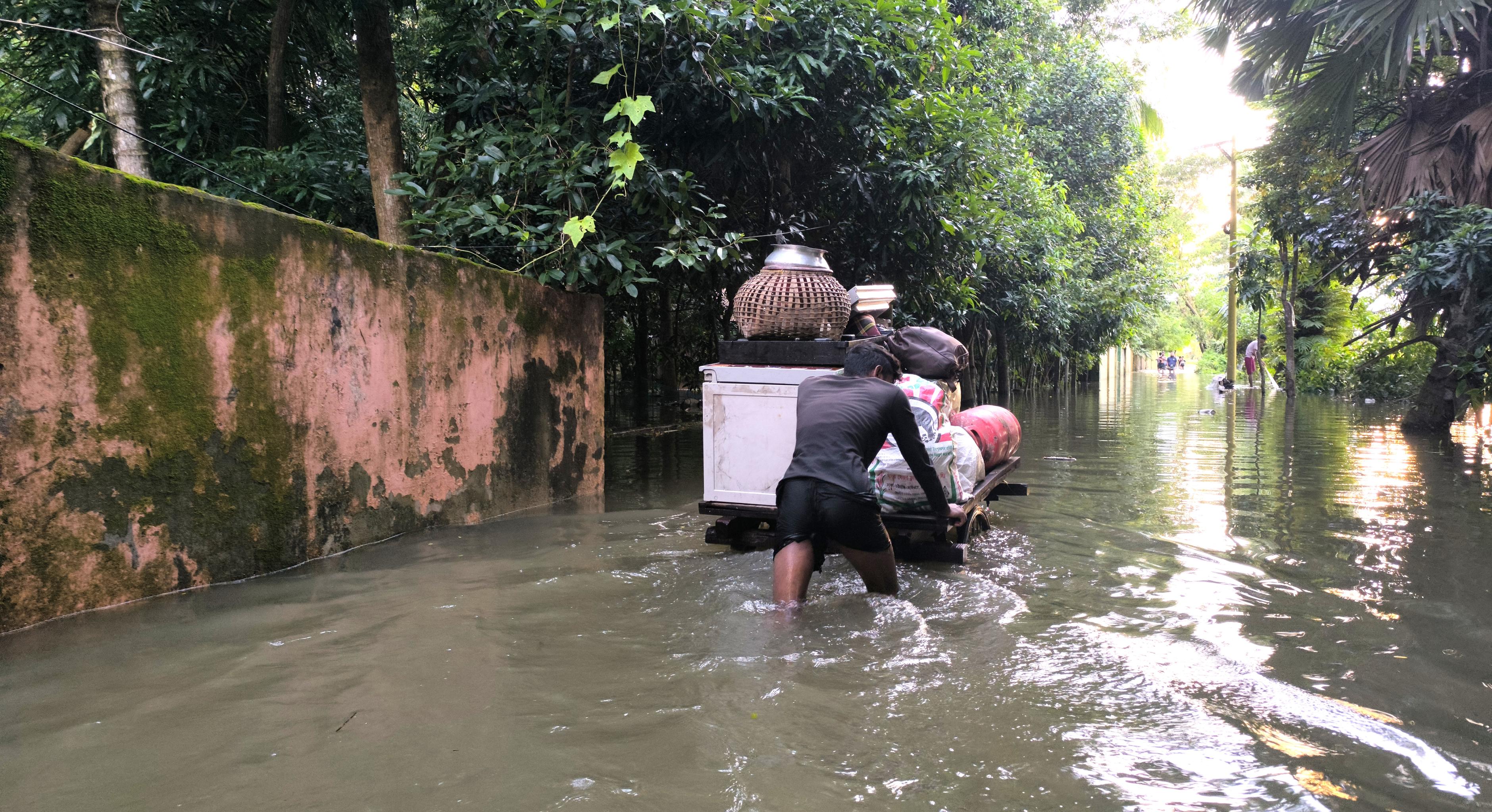 Ein Mensch schiebt sein Hab und Gut auf einem Wagen durch knietiefes Wasser