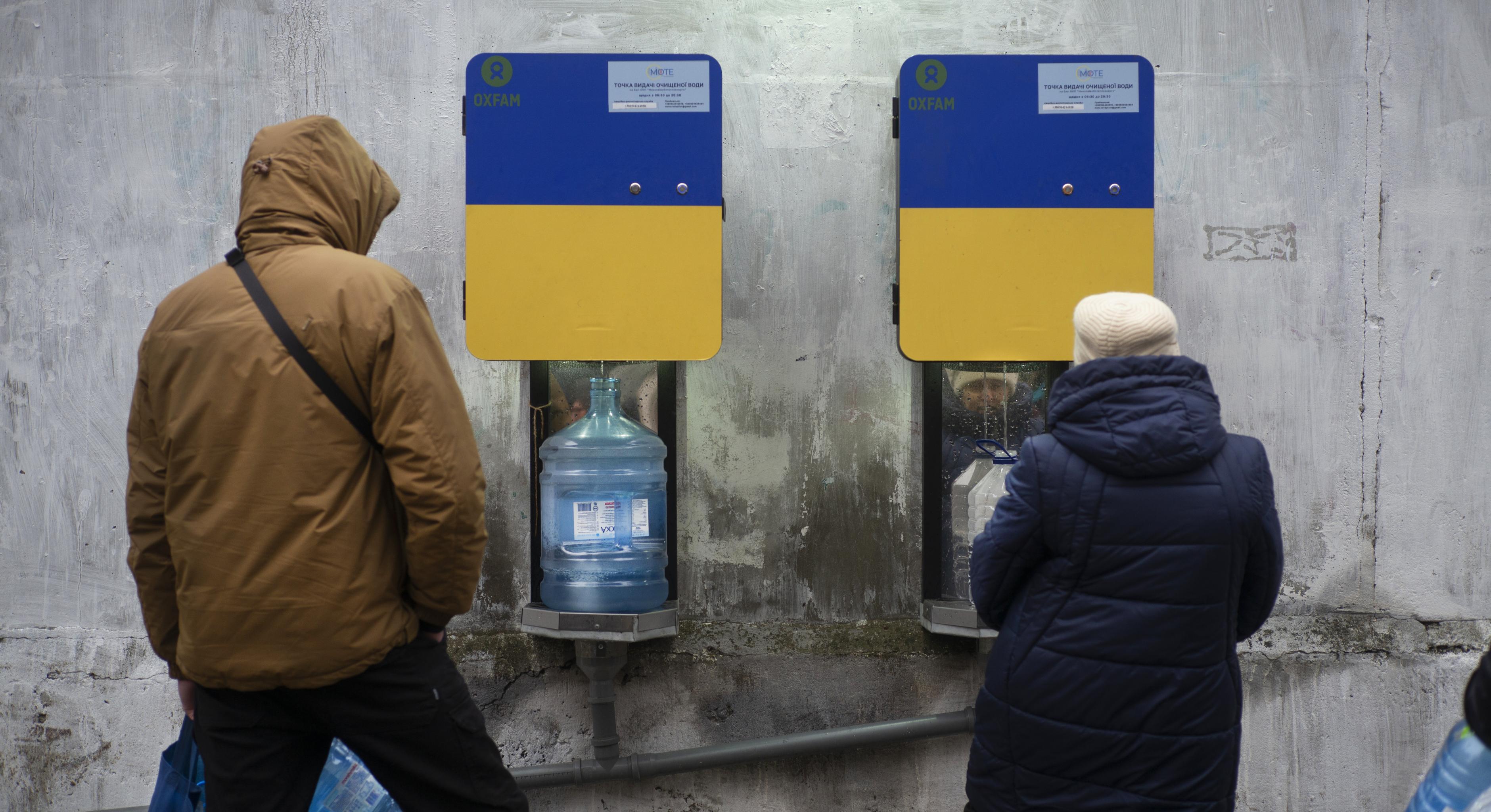 Zwei Personen holen Wasser an einer Wasserstelle von Oxfam. In der Stadt Mykolaiv wird Trinkwasser bereitgestellt, weil die Wasserleitungen in den Häusern zerstört wurden.