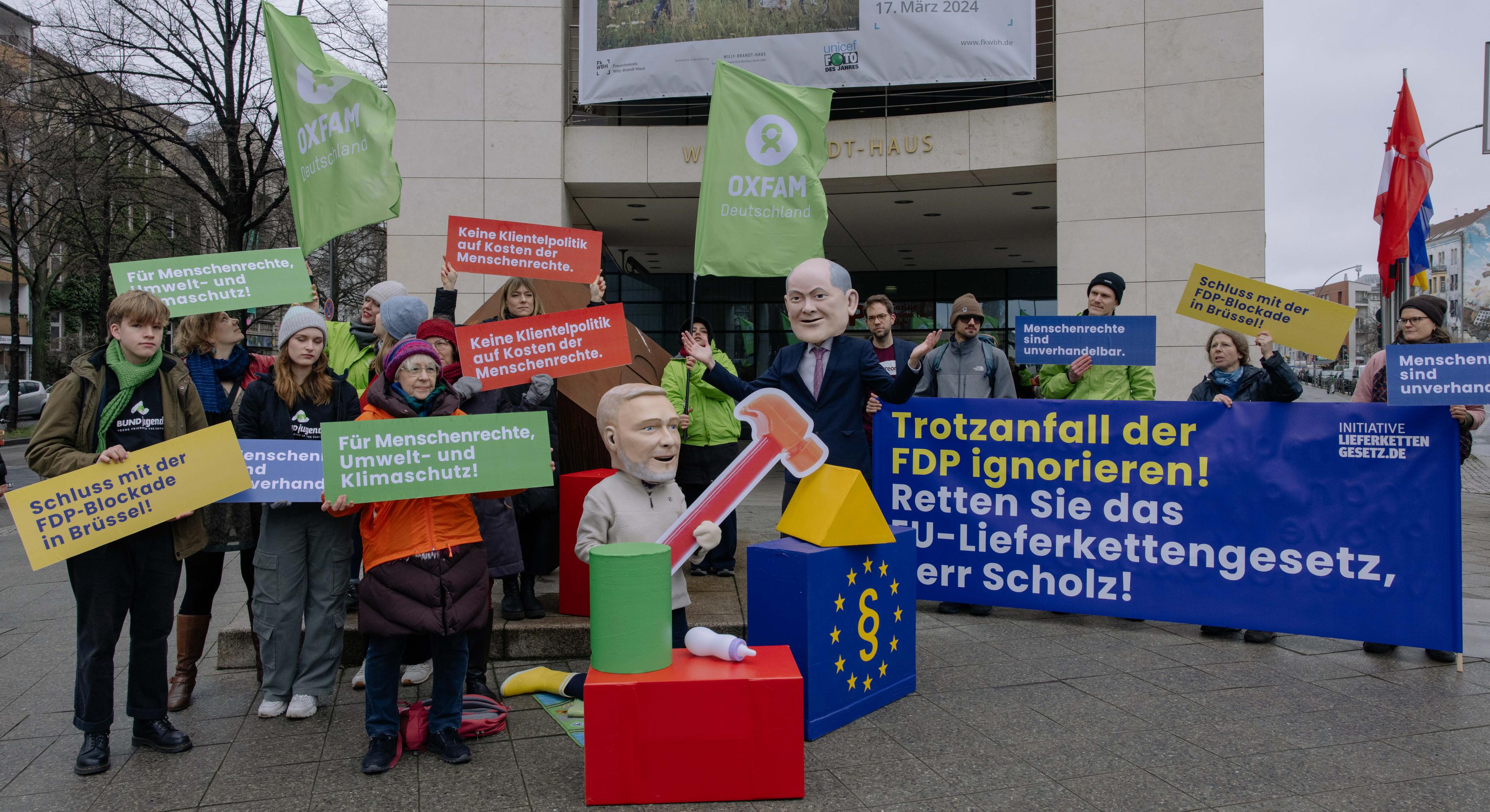 Vor dem Willy-Brandt-Haus stellen als Christian Lindner und Olaf Scholz verkleidete Aktivist*innen einen FDP-Trotzanfall dar und fordern vom Kanzler: "Trotzanfall der FDP ignorieren! Retten Sie das EU-Lieferkettengesetz, Herr Scholz!"