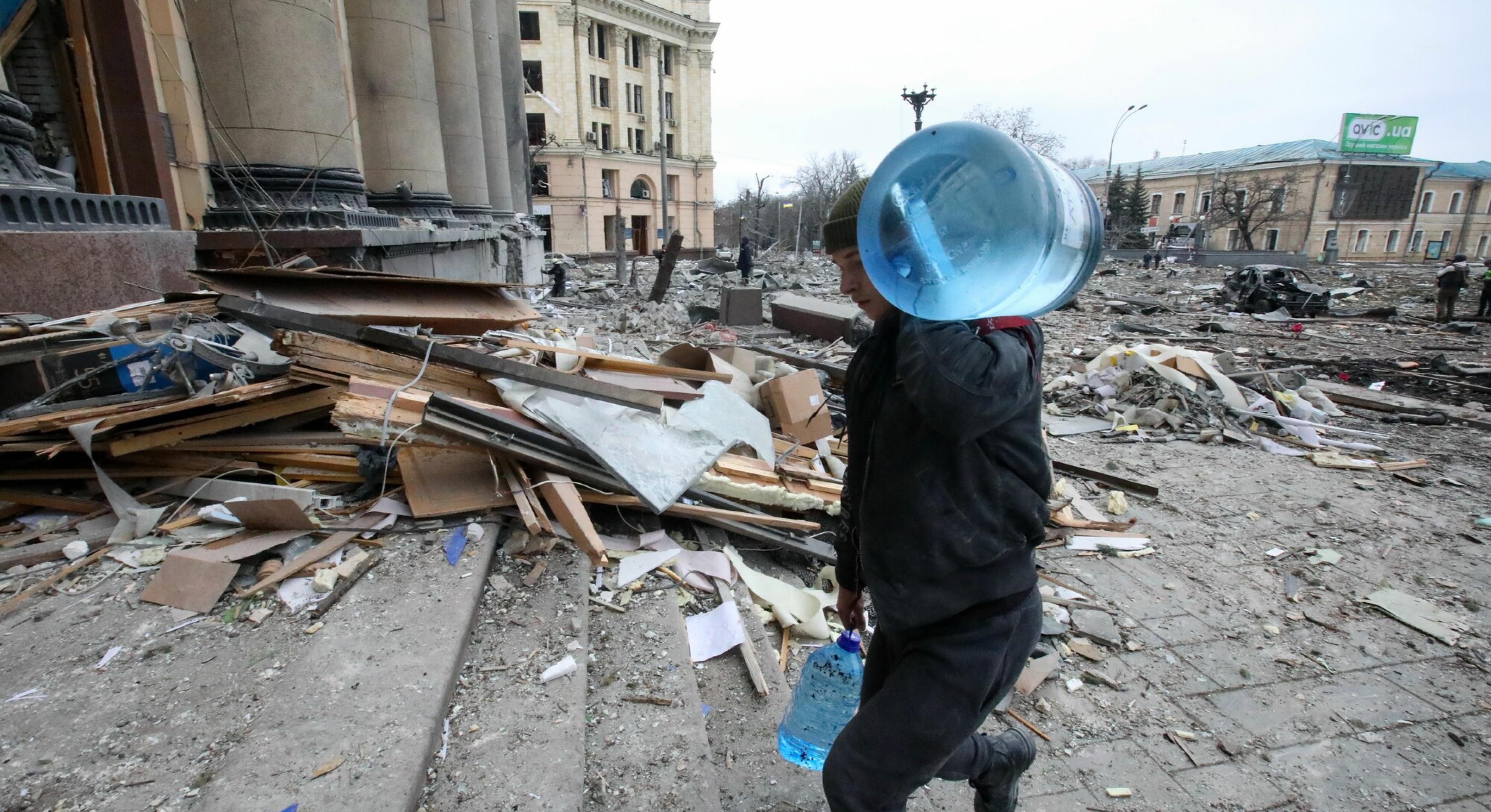 Ein Mann trägt Wasserbehälter in das beschädigte Gebäude der staatlichen Regionalverwaltung von Charkiw, Ukraine
