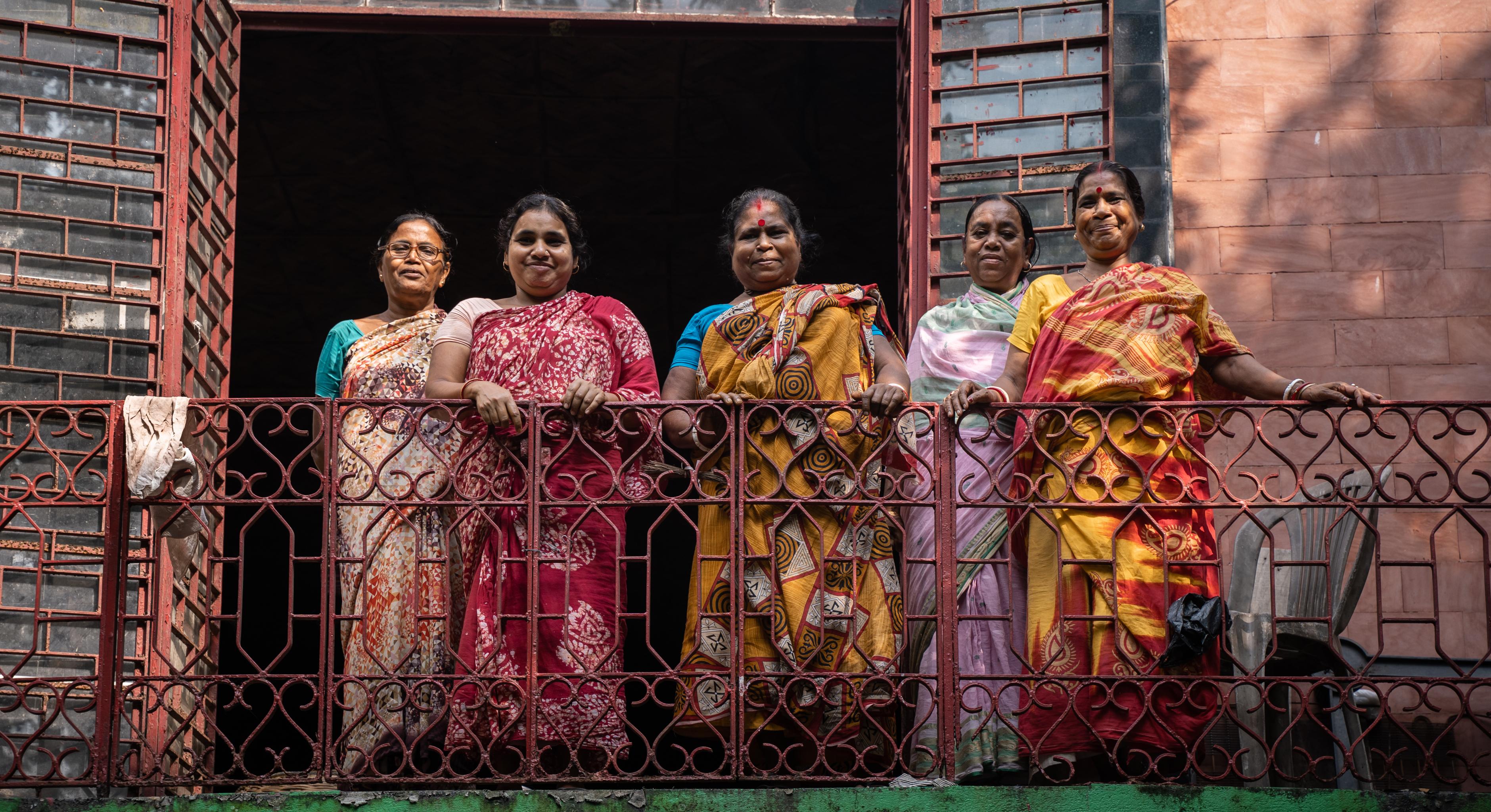 Frauen in bunten Saris stehen auf einem Balkon und lächeln in die Kamera