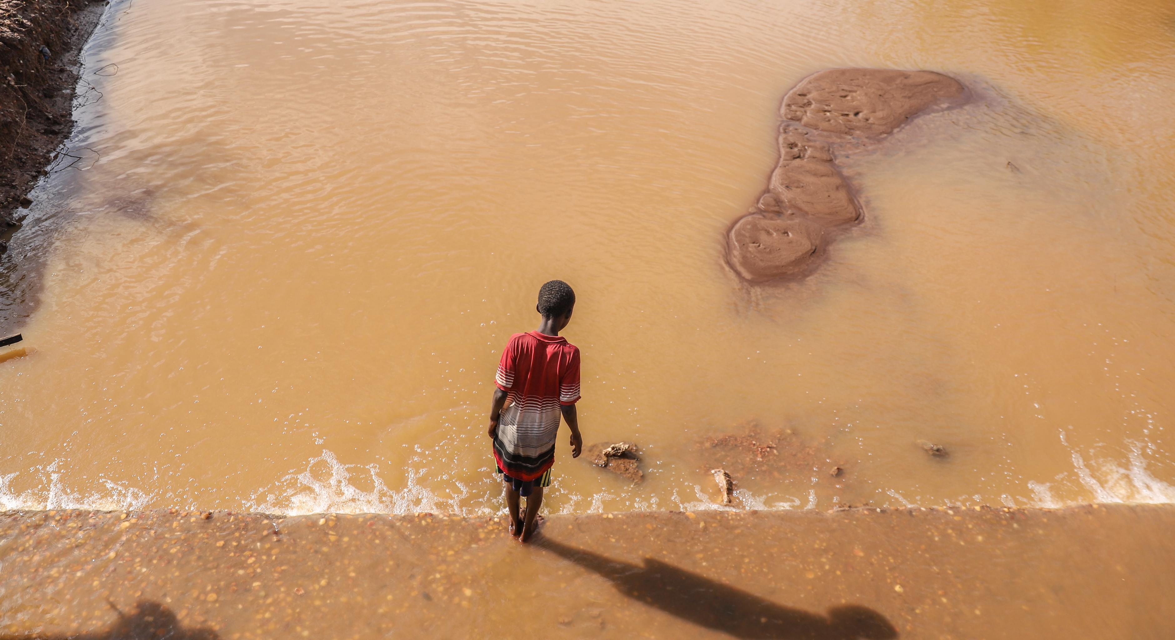 Ein Kind steht auf einer Brücke, die von Wasser bedeckt ist und schaut hinunter