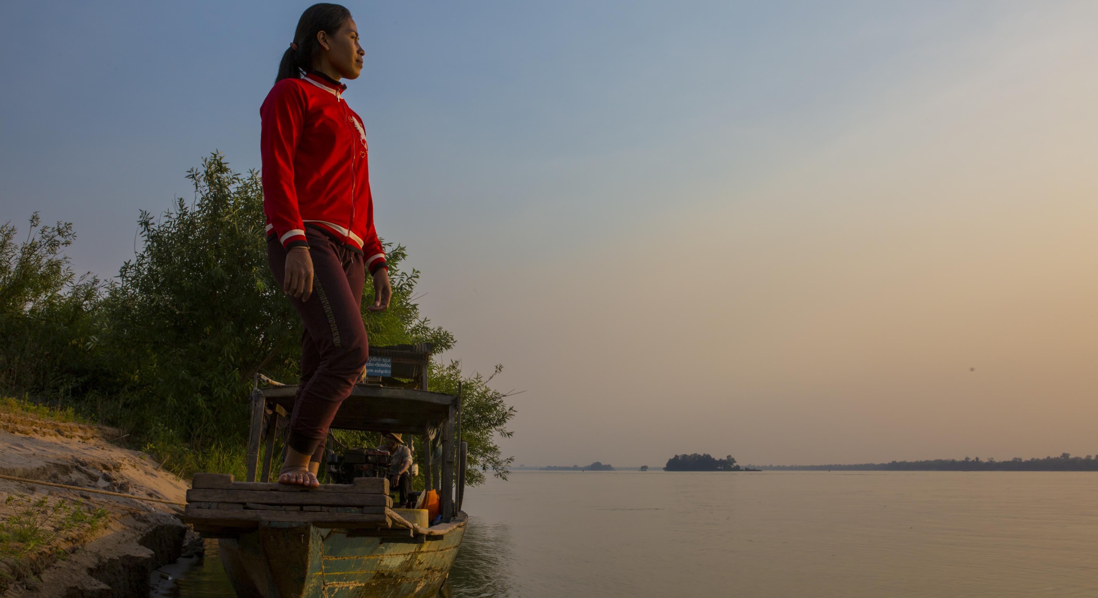 Eine Frau steht auf einem Boot und blickt über das Wasser in die Ferne