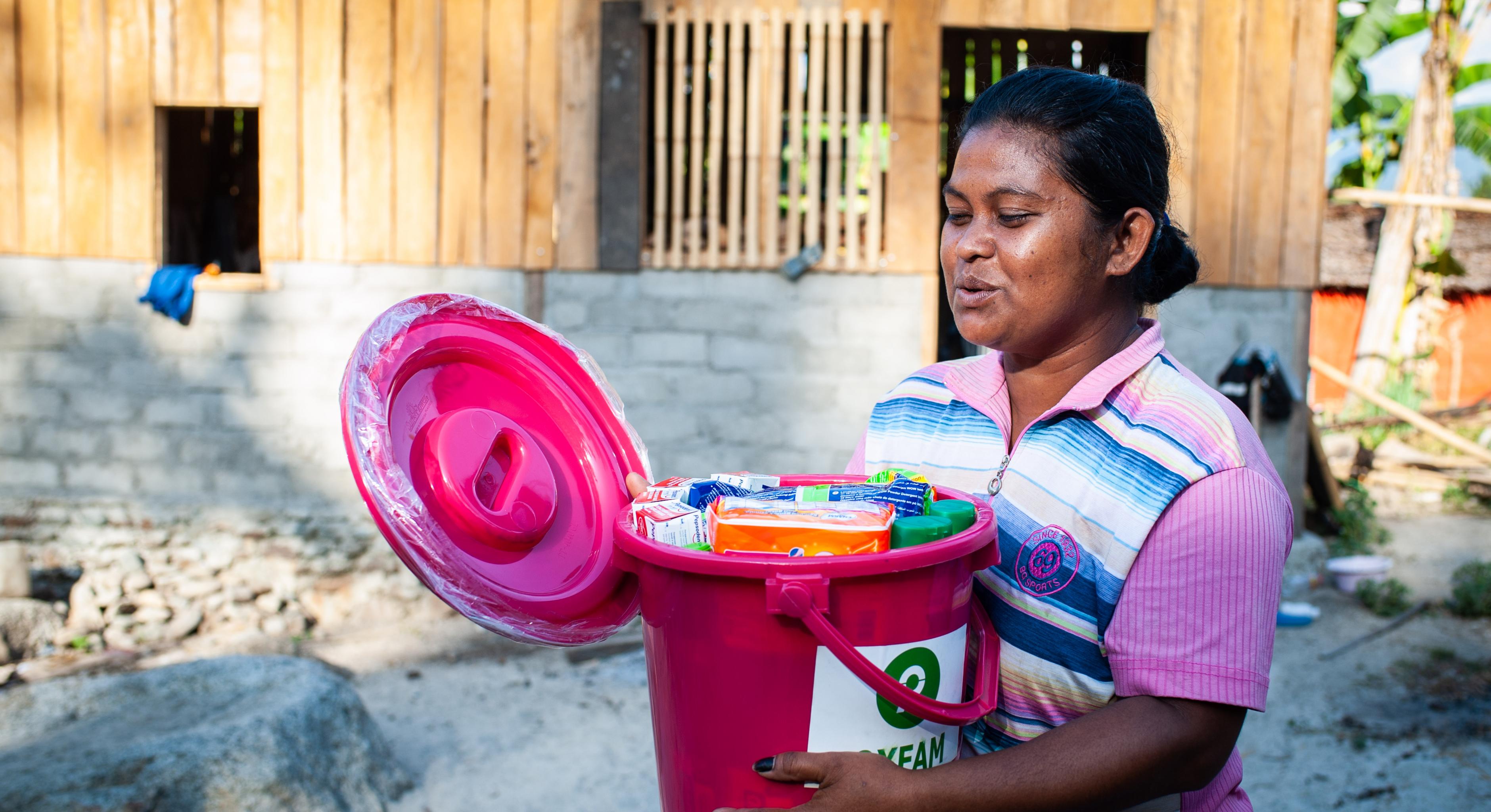 Eine Frau öffnet einen Oxfam-Plastikeimer, der mit Hygieneartikeln gefüllt ist.