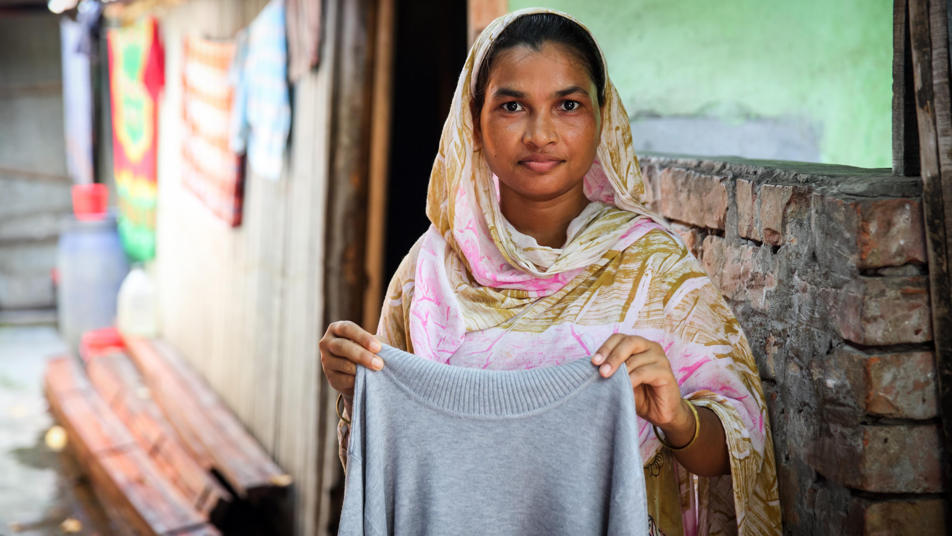Die Textilarbeiterin Anju hält ein Kleidungsstück, das sie genäht hat.