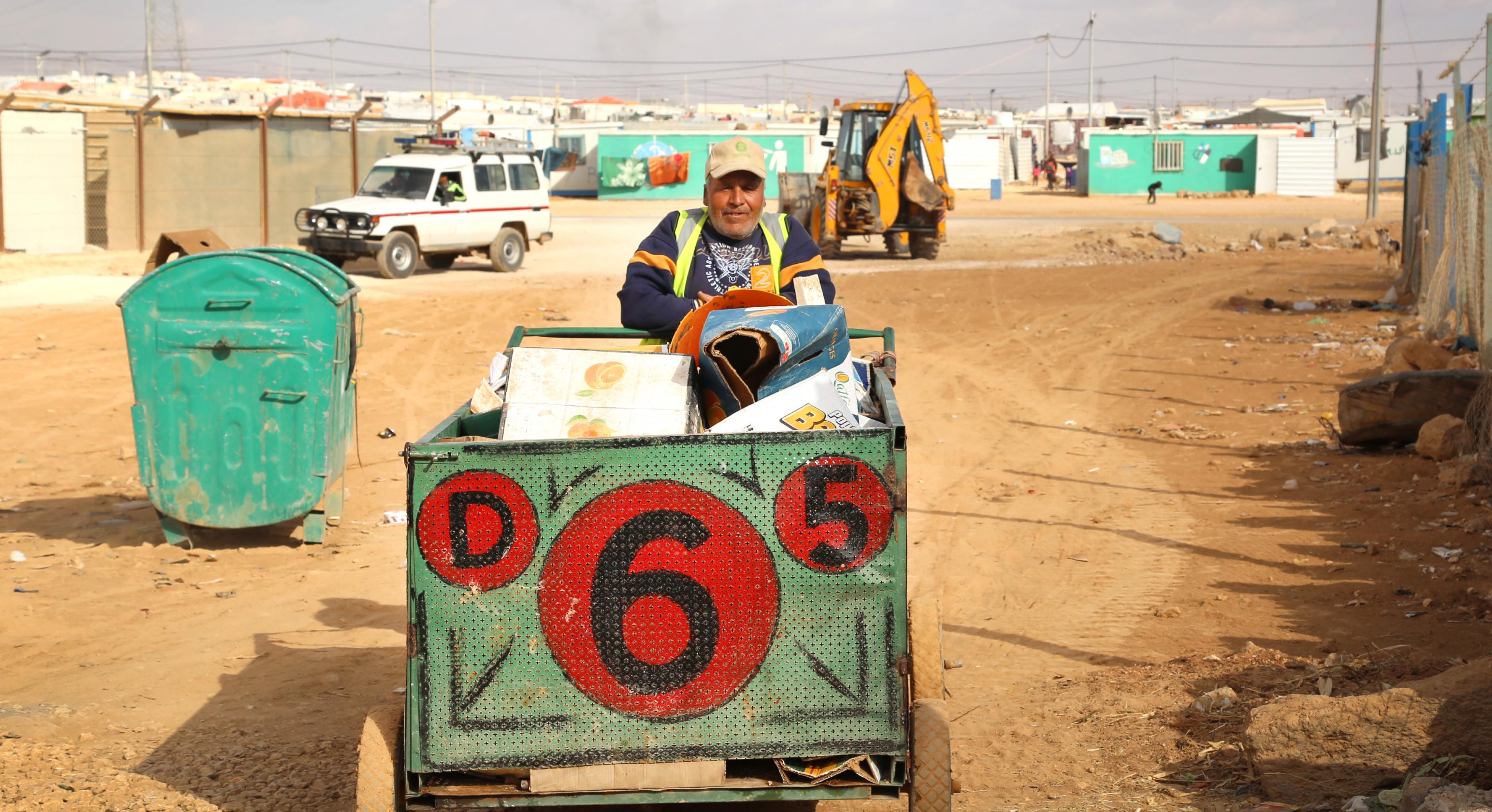 Ein Mann mit Oxfam-Mütze sammelt Abfall in einem Karren.