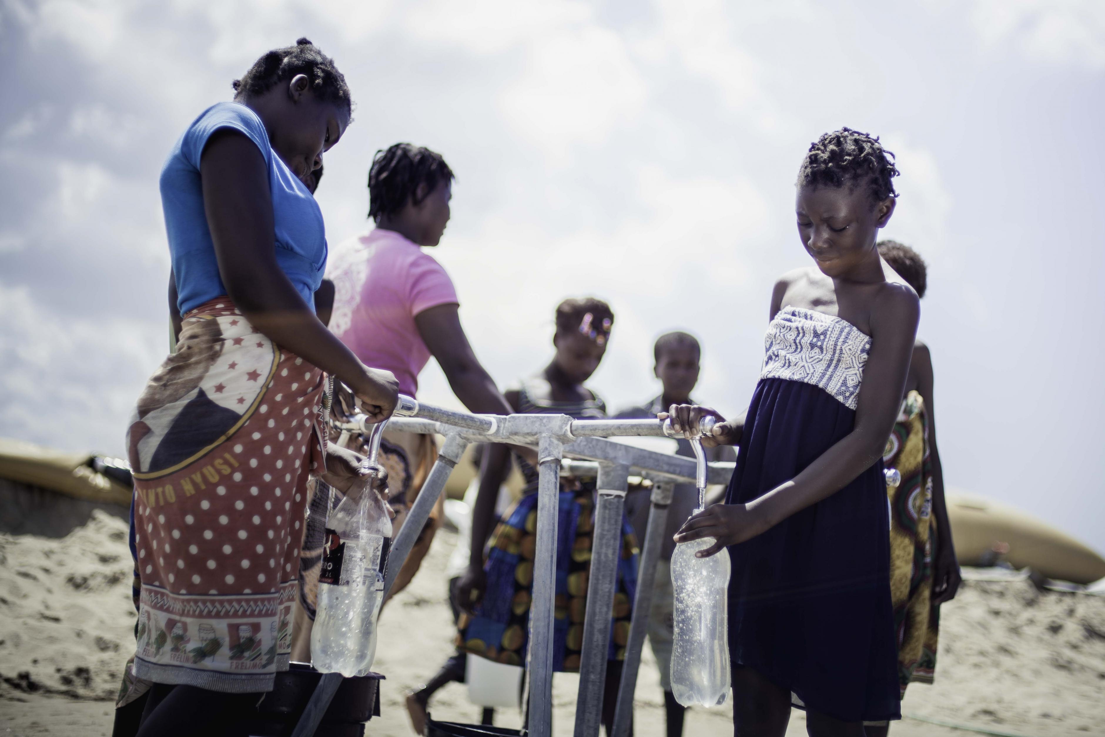 Frauen und Mädchen füllen Wasserflaschen an einer Wasserstelle