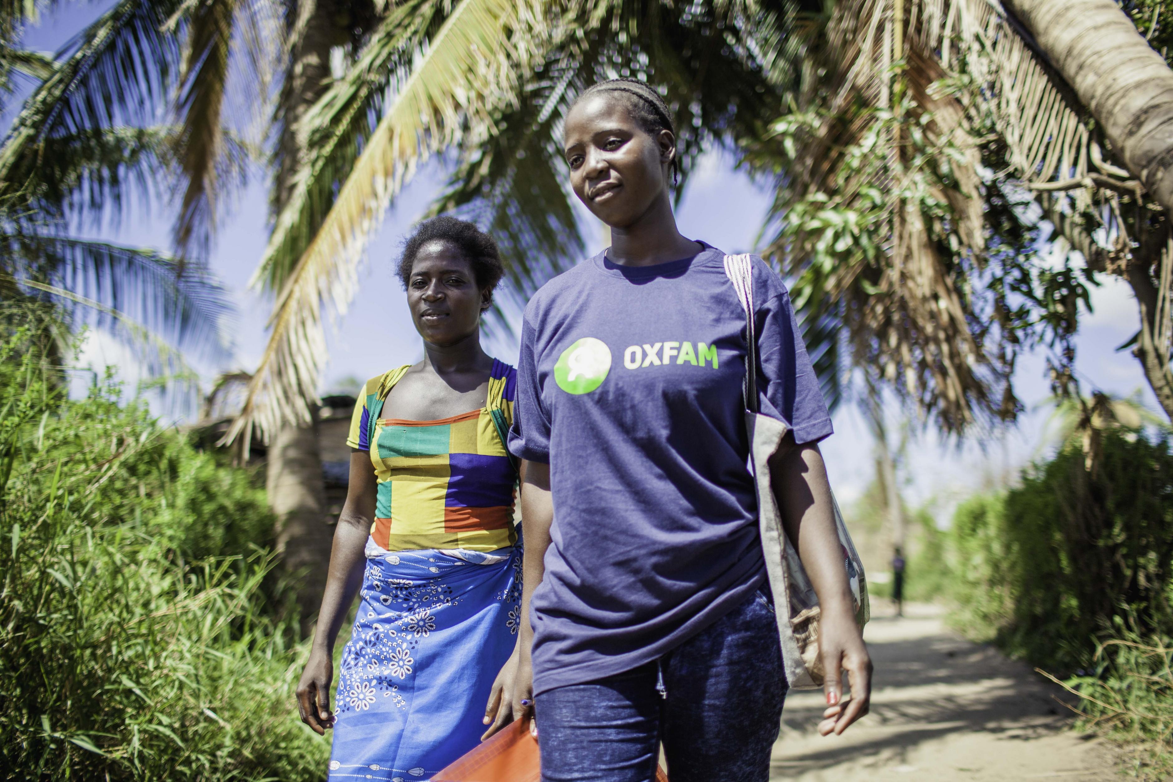 Zwei Frauen gehen unter einer Palme, eine trägt ein Oxfam-T-Shirt