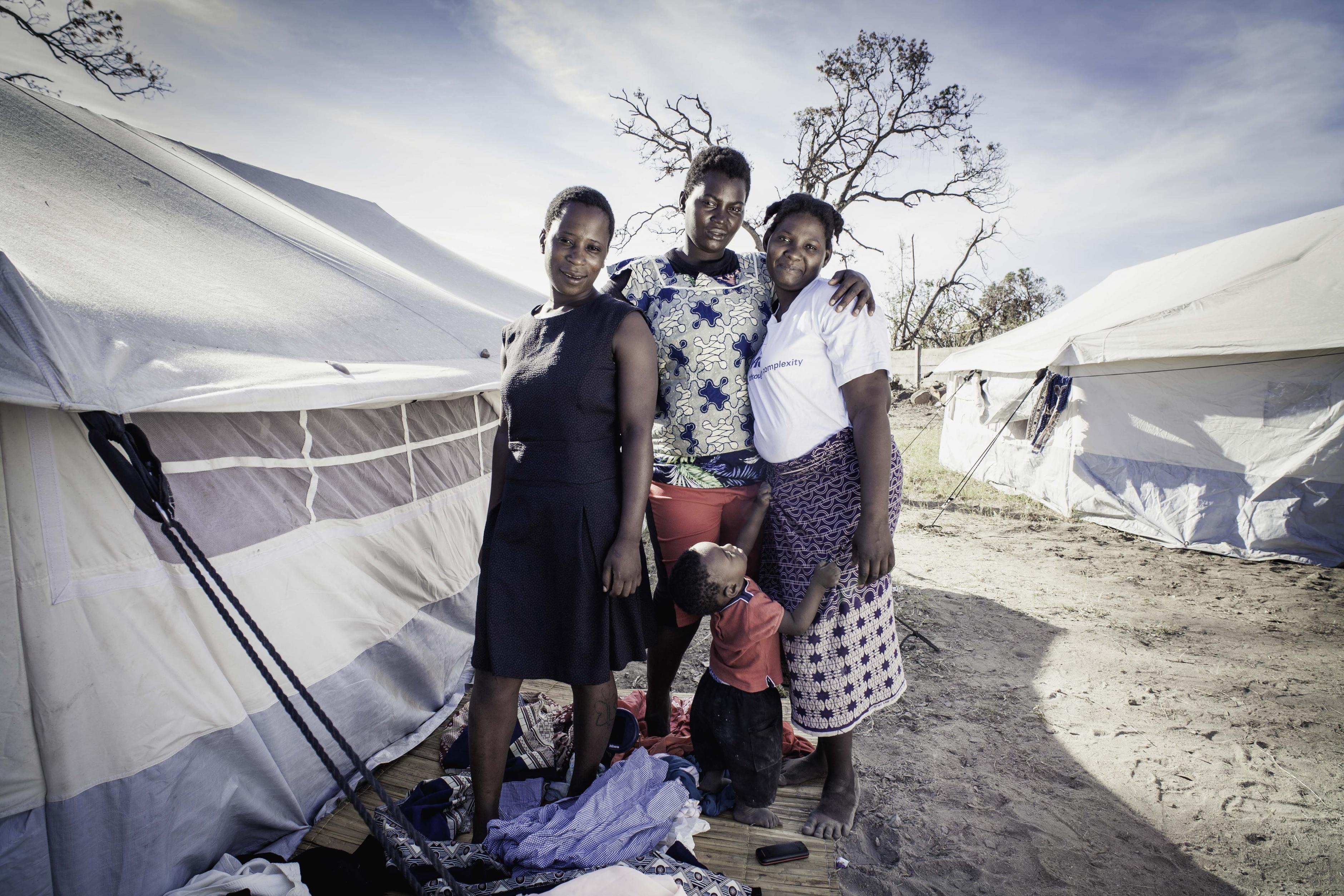 Drei Frauen und ein Kind stehen inmitten von Kleidung neben einem Zelt