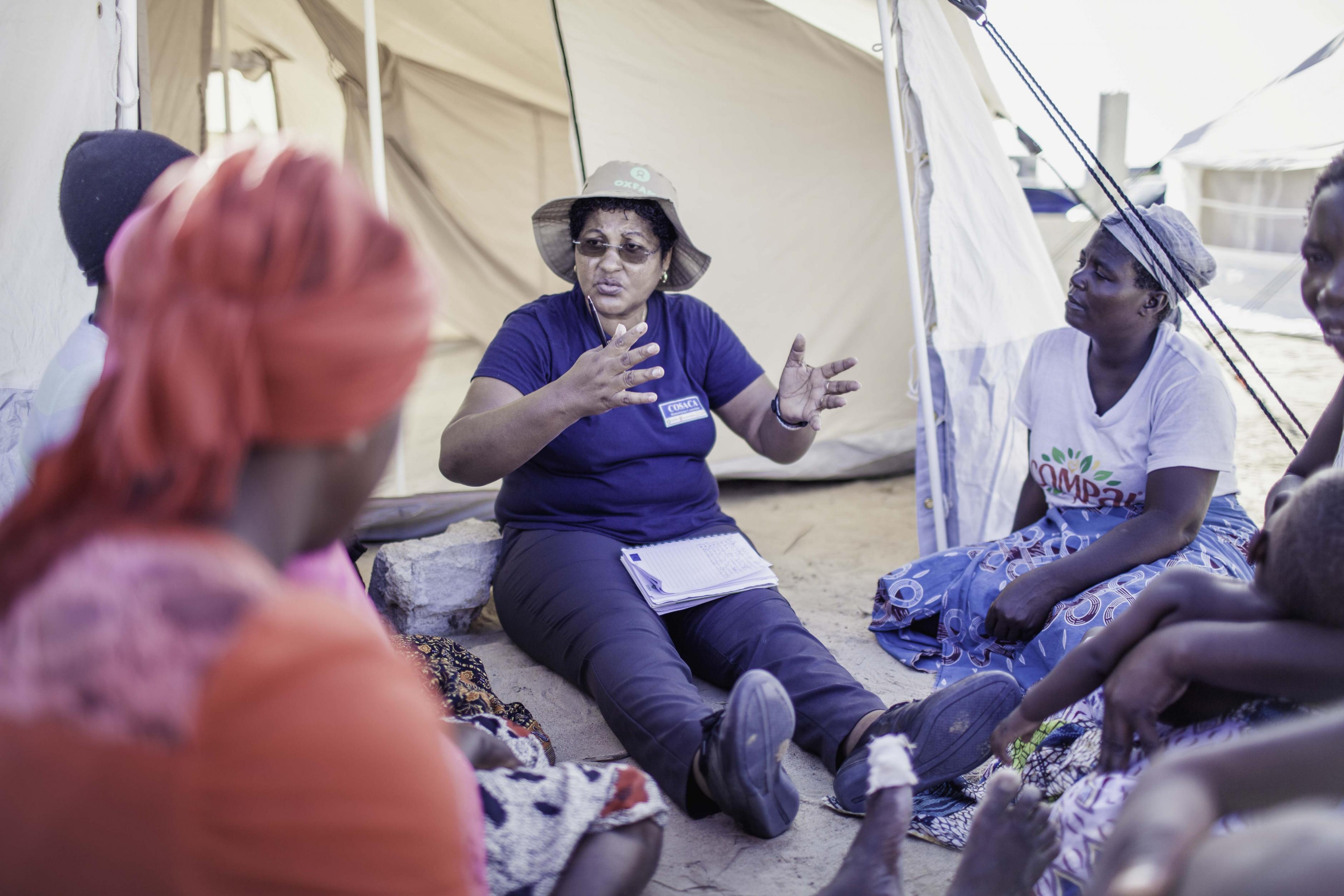 Eine Gruppe von Frauen sitzt auf dem Boden vor einem Zelt und berät sich.