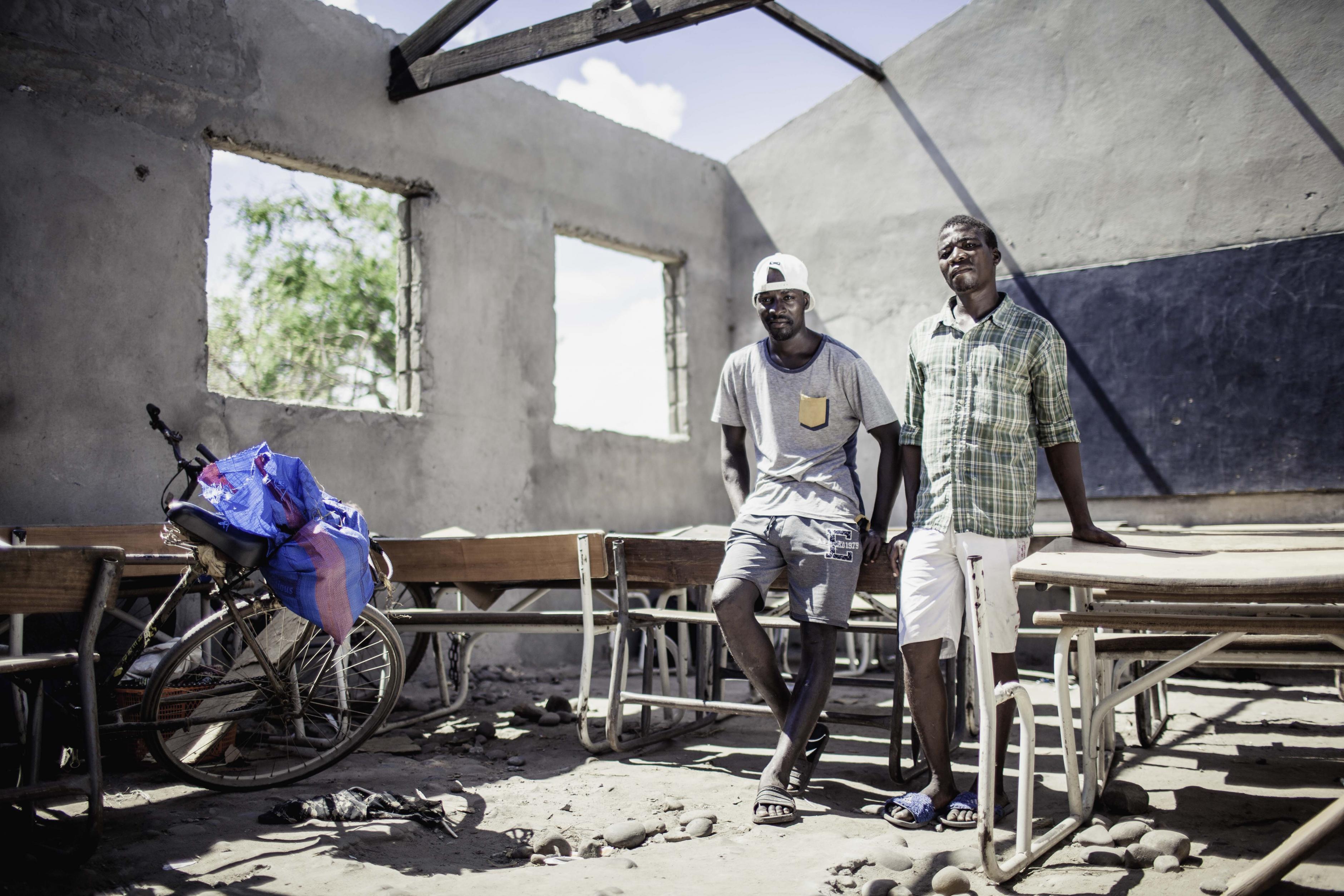 Zwei Männer stehen in einem zerstörten Klassenzimmer ohne Dach.