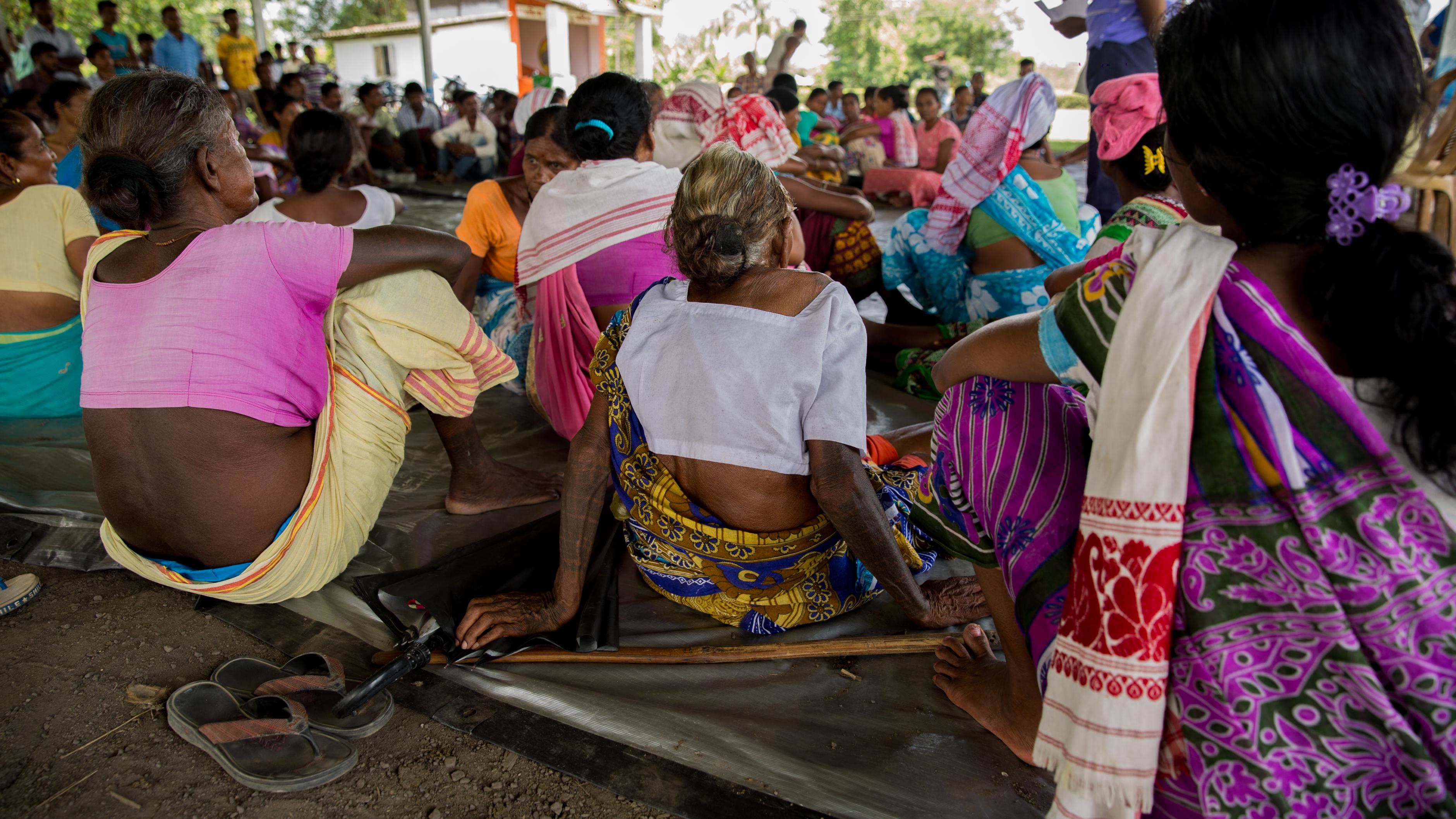 Frauen in bunten Saris sitzen im Halbkreis auf dem Boden und verfolgen einen Vortrag