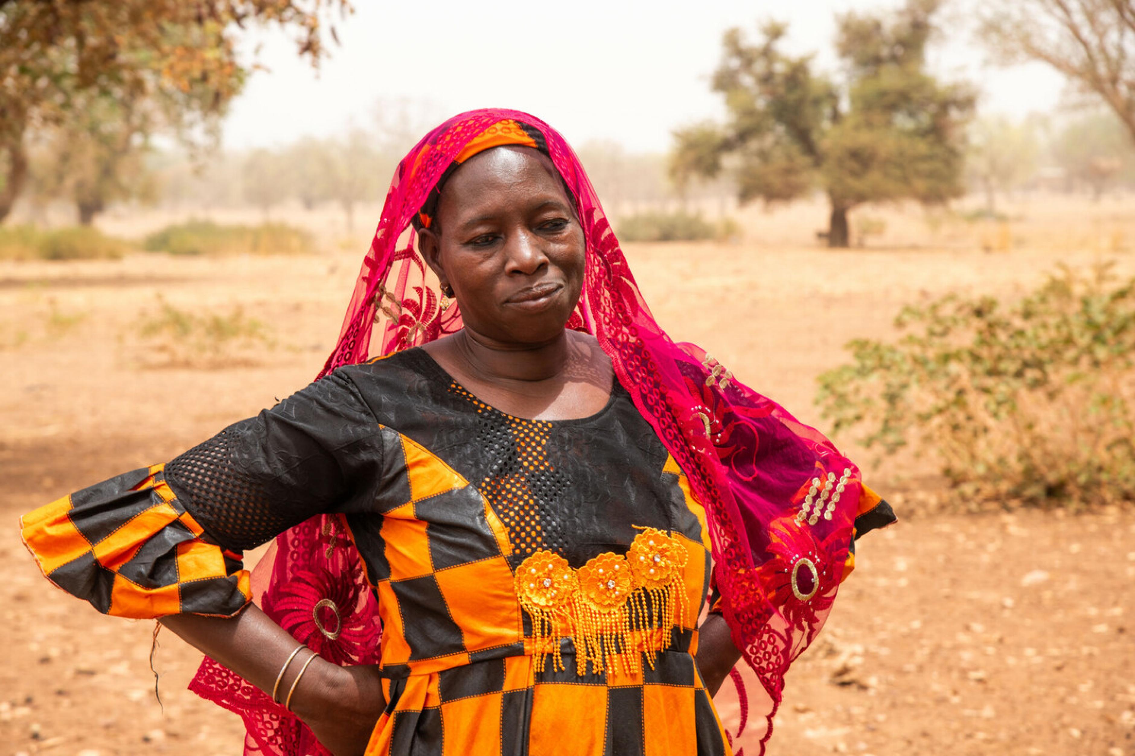 Sanfo Ramata ist Bäuerin und Viehzüchterin. Sie arbeitet für die Confédération Paysanne du Faso, eine Partnerorganisation von Oxfam. Die Frau steht in einem bunten Kleid vor einem Haus. Sie sieht nachdenklich aus.