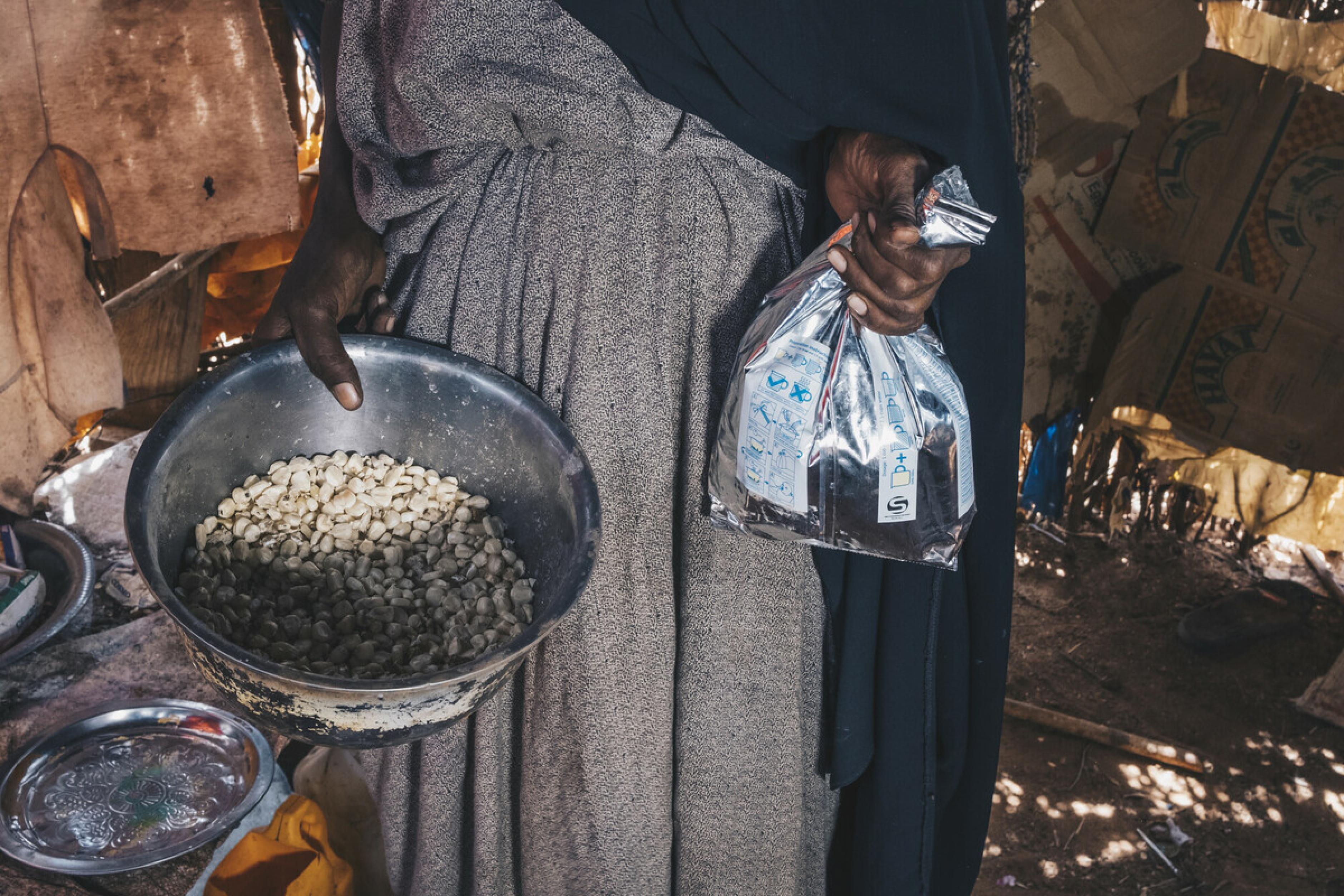 Diyaara* zeigt die Lebensmittel, die sie noch hat, um für ihre Familie zu kochen und ihr verbliebenes Vieh zu füttern. Sie zeigt eine Schüssel, deren Boden bedeckt ist, und einen kleinen Beutel, der etwa halbvoll ist. Sie lebt in Wajir, Kenia, wo derzeit eine Hungerkrise herrscht.