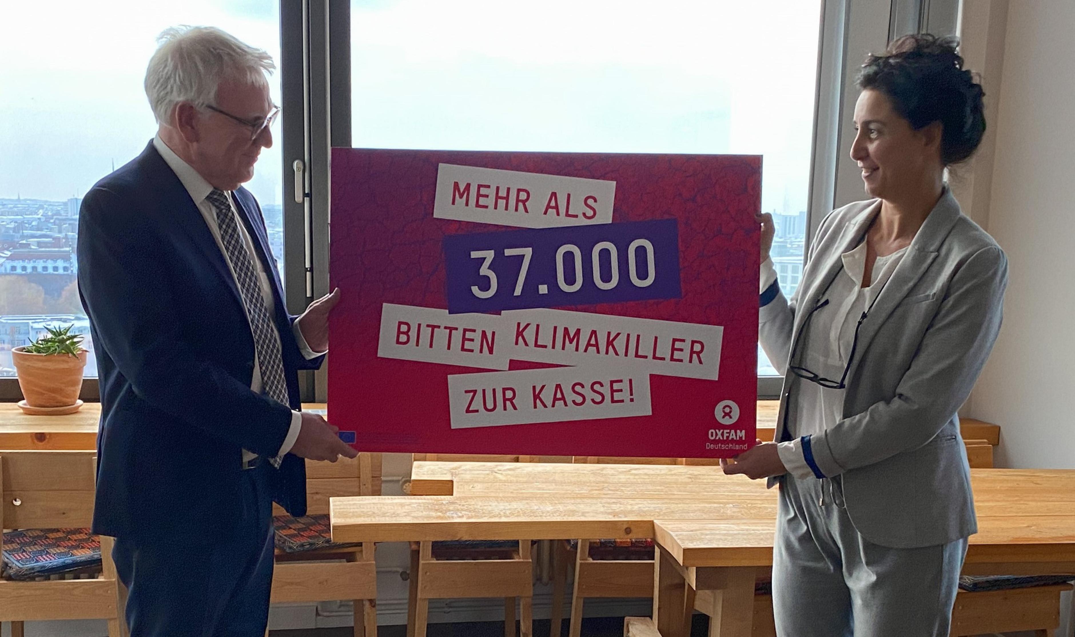 Zwei Menschen halten ein Schild hoch, auf dem steht: Mehr als 37.000 bitten Klimakiller zur Kasse. Dies bezieht sich auf eine Unterschriftenaktion, die Aufmerksamkeit auf eine gerechte Klimapolitik lenken soll.