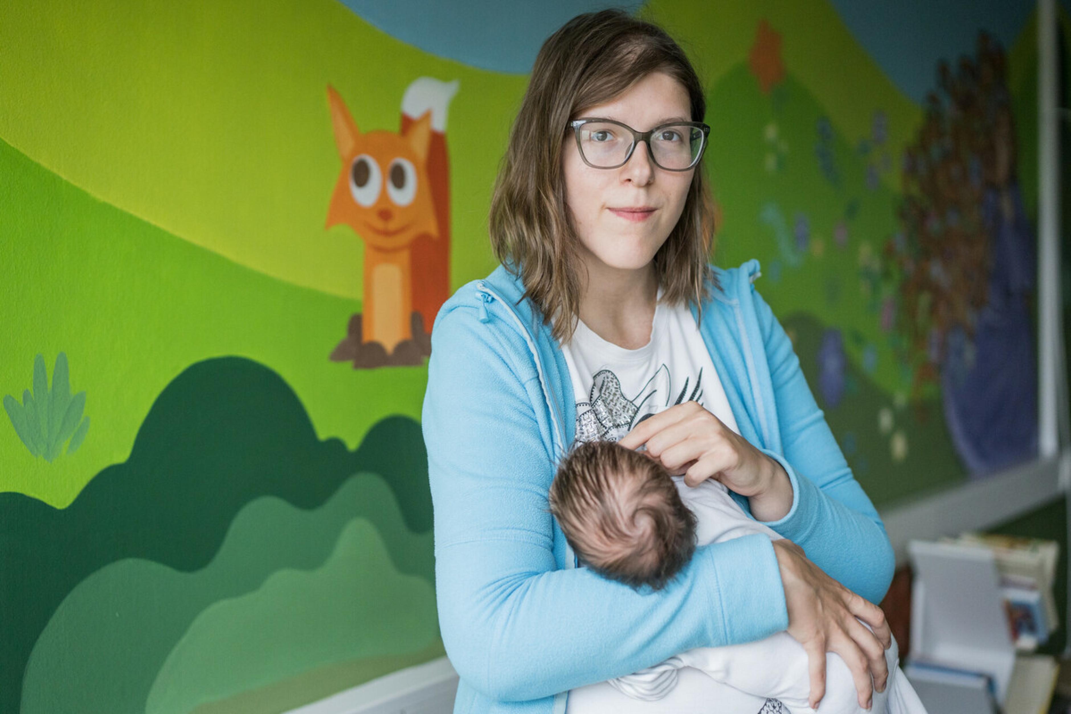Olga hält ihre einen Monat alte Tochter Zlata* auf dem Arm. Sie sitzt vor einer bunt bemalten Wand mit Tiermotiv.