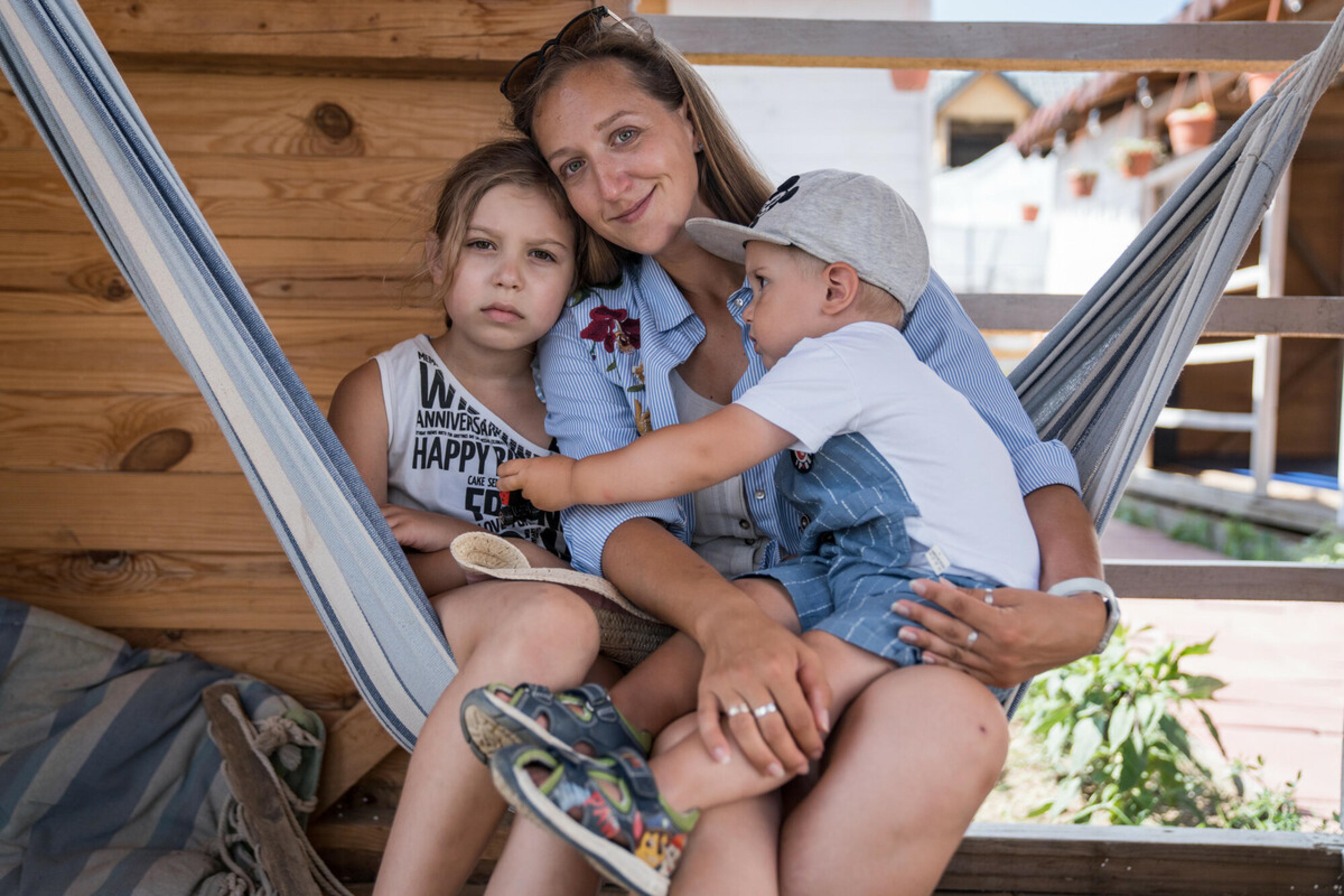 Katerina*, eine Geflüchtete aus der Ukraine, zusammen mit ihrer Tochter Daria* und ihrem Sohn Miron*. Sie sitzen in einer Hängematte in einem Spielhaus und wirken freundlich, aber ernst..