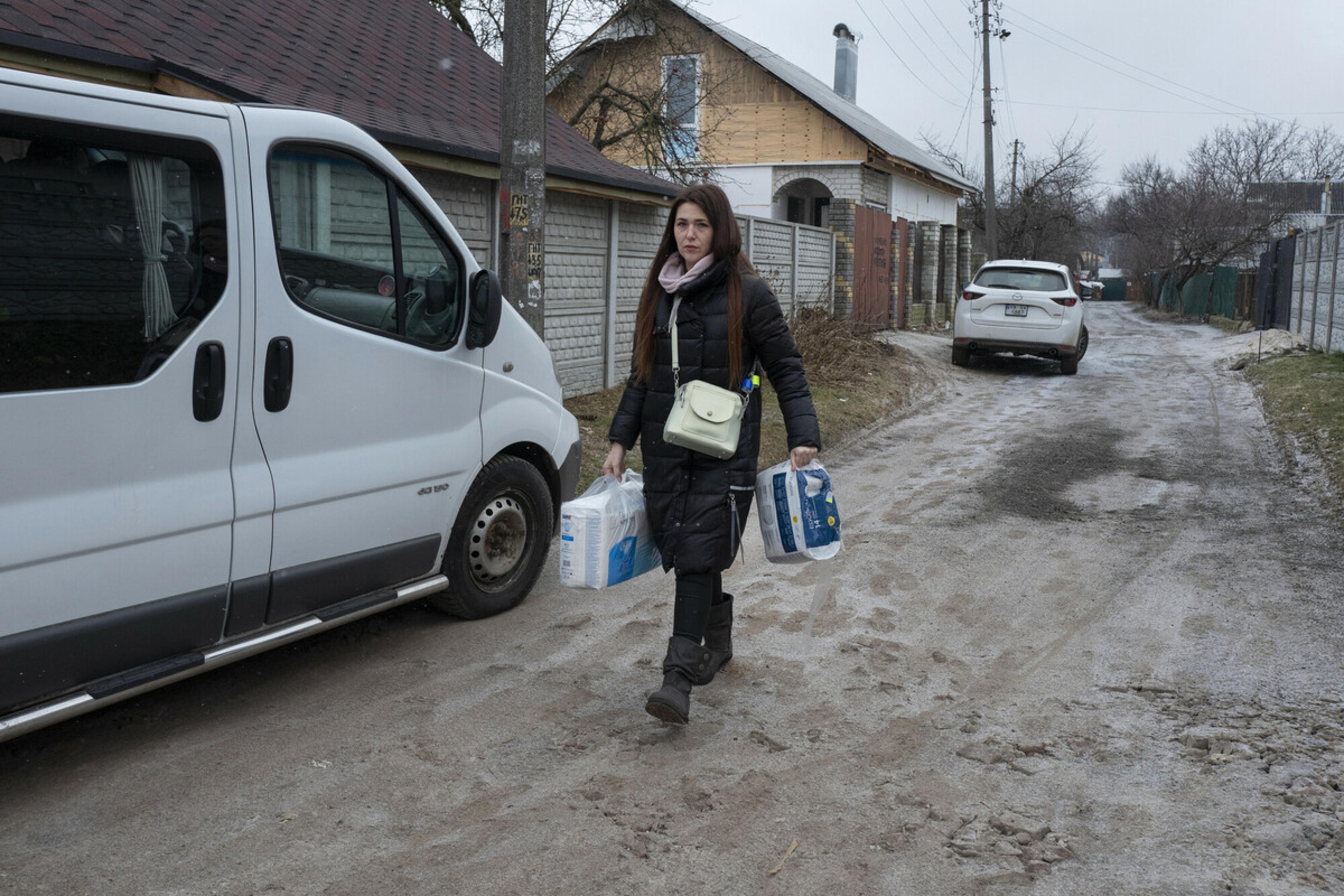 Anna Kuljewa läuft eine matschige Straße entlang. Sie trägt Tüten mit Hygieneartikeln.