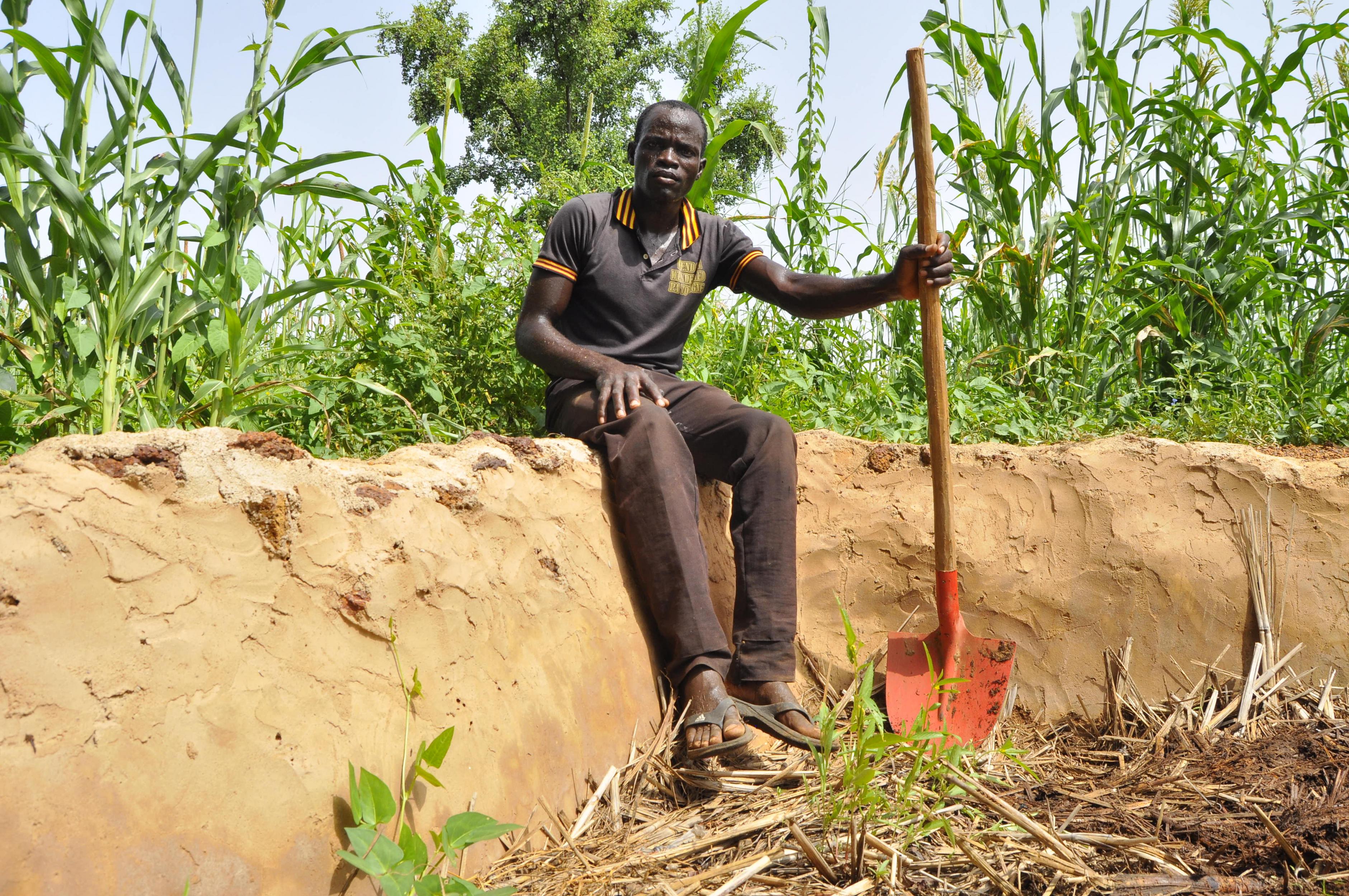 Bauer Marou Sebgo sitzt mit einem Spaten neben einer Kompostgrube.