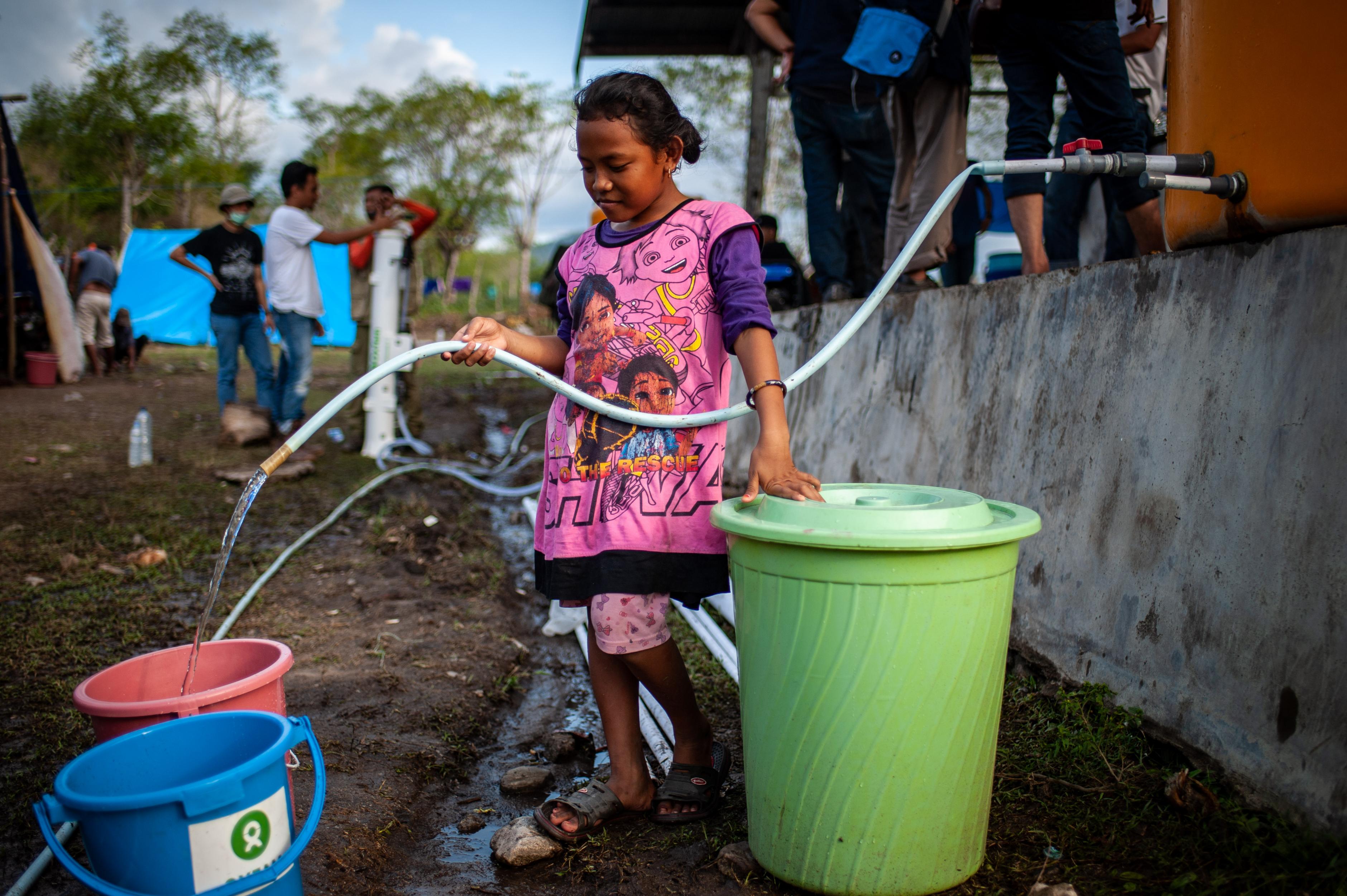 Ein Mädchen füllt Wasser aus einem Fass in einen Eimer.