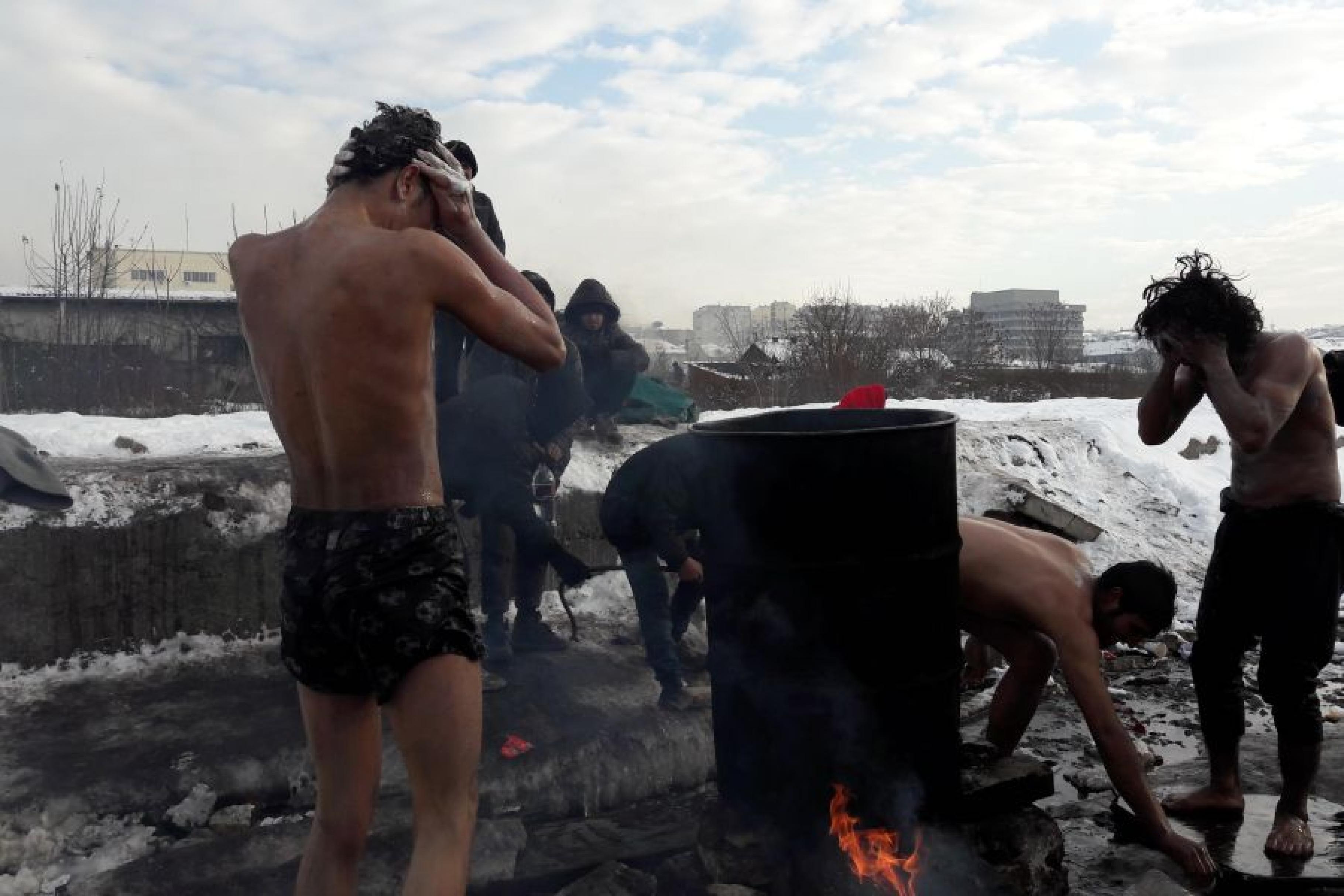 Männer stehen auf einer schneebedeckten Brachfläche um eine Feuertonne und waschen sich 