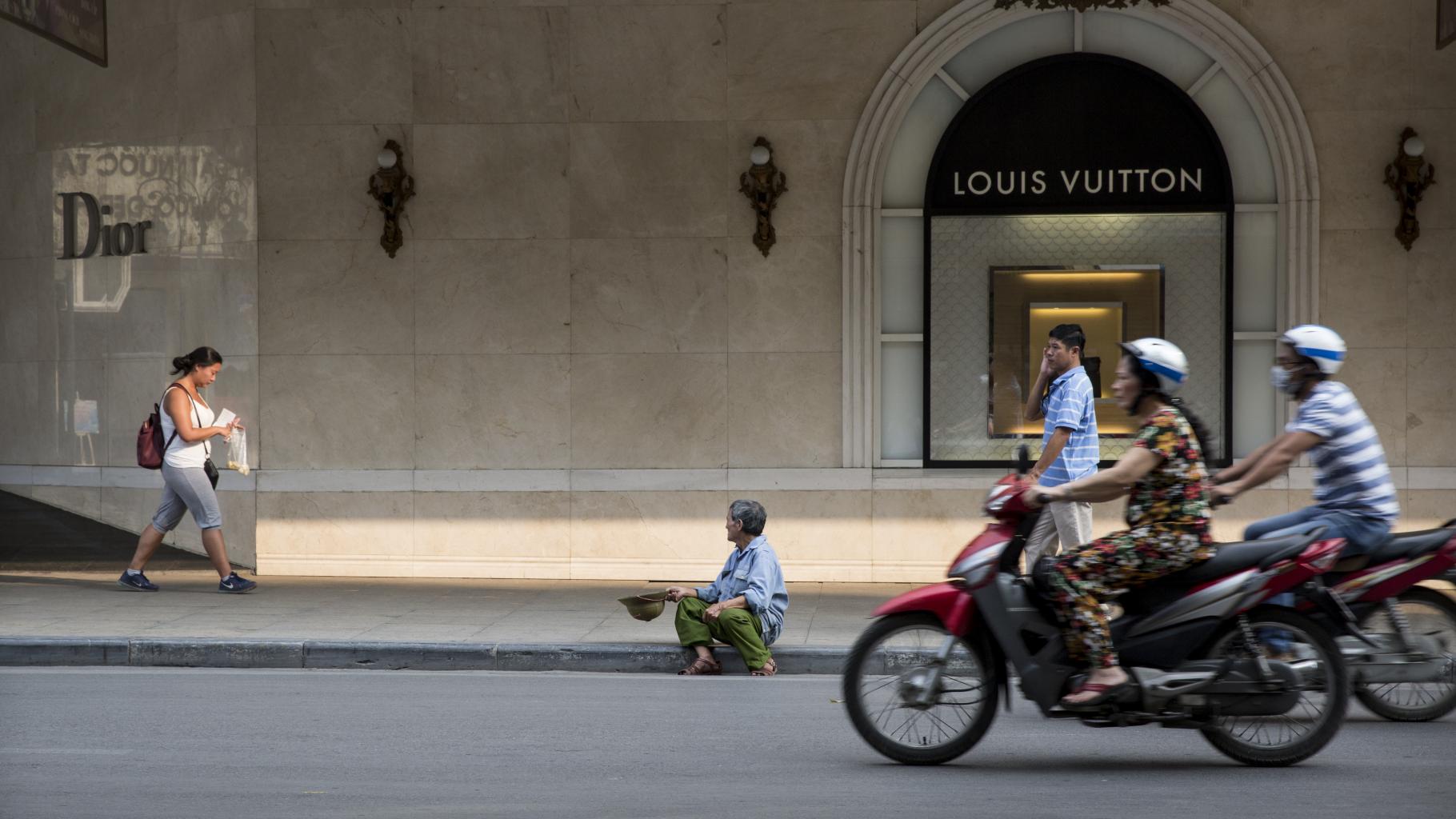 Mann sitzt vor Louis-Vuitton-Laden in Hanoi und bettelt
