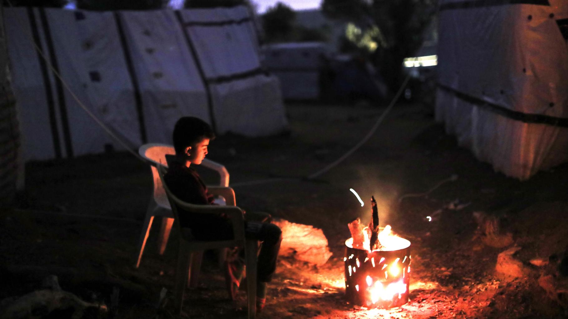 Ein Junge sitzt in einem Flüchtlingscamp vor einem kleinen Feuer