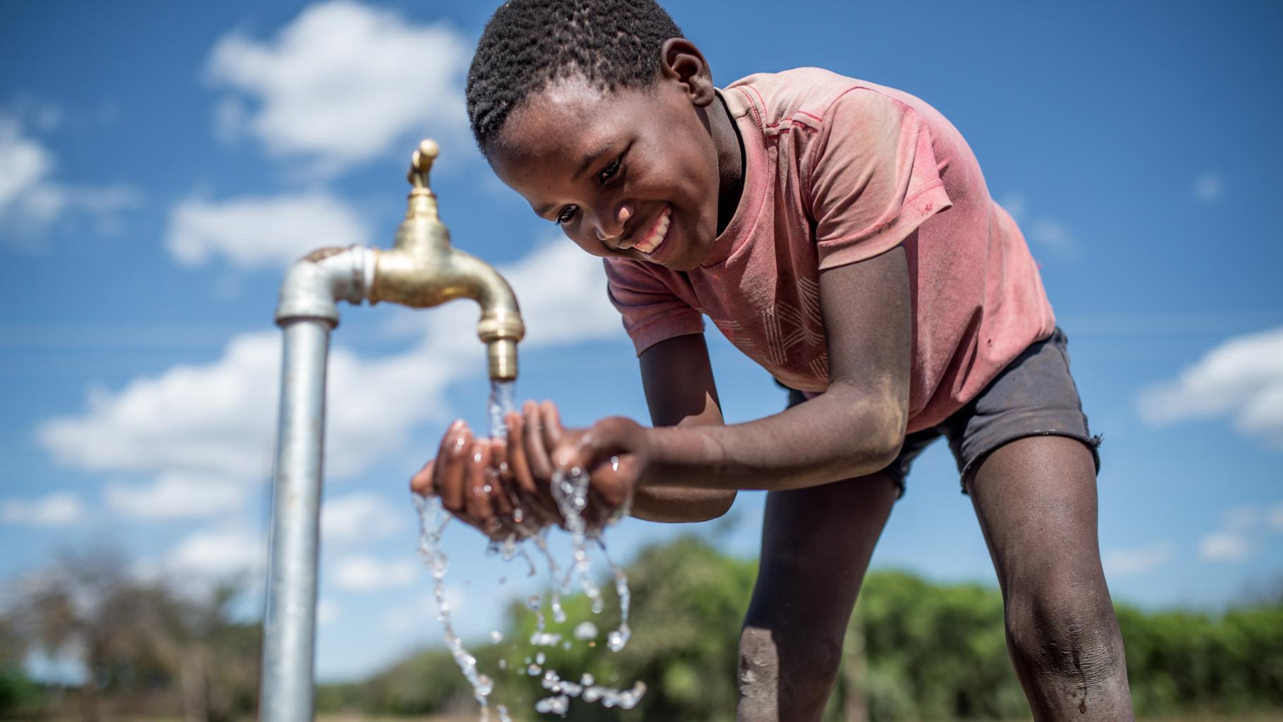 Purity (Name geändert) aus Simbabwe trinkt Wasser aus einem von Oxfam installierten Wasserhahn.