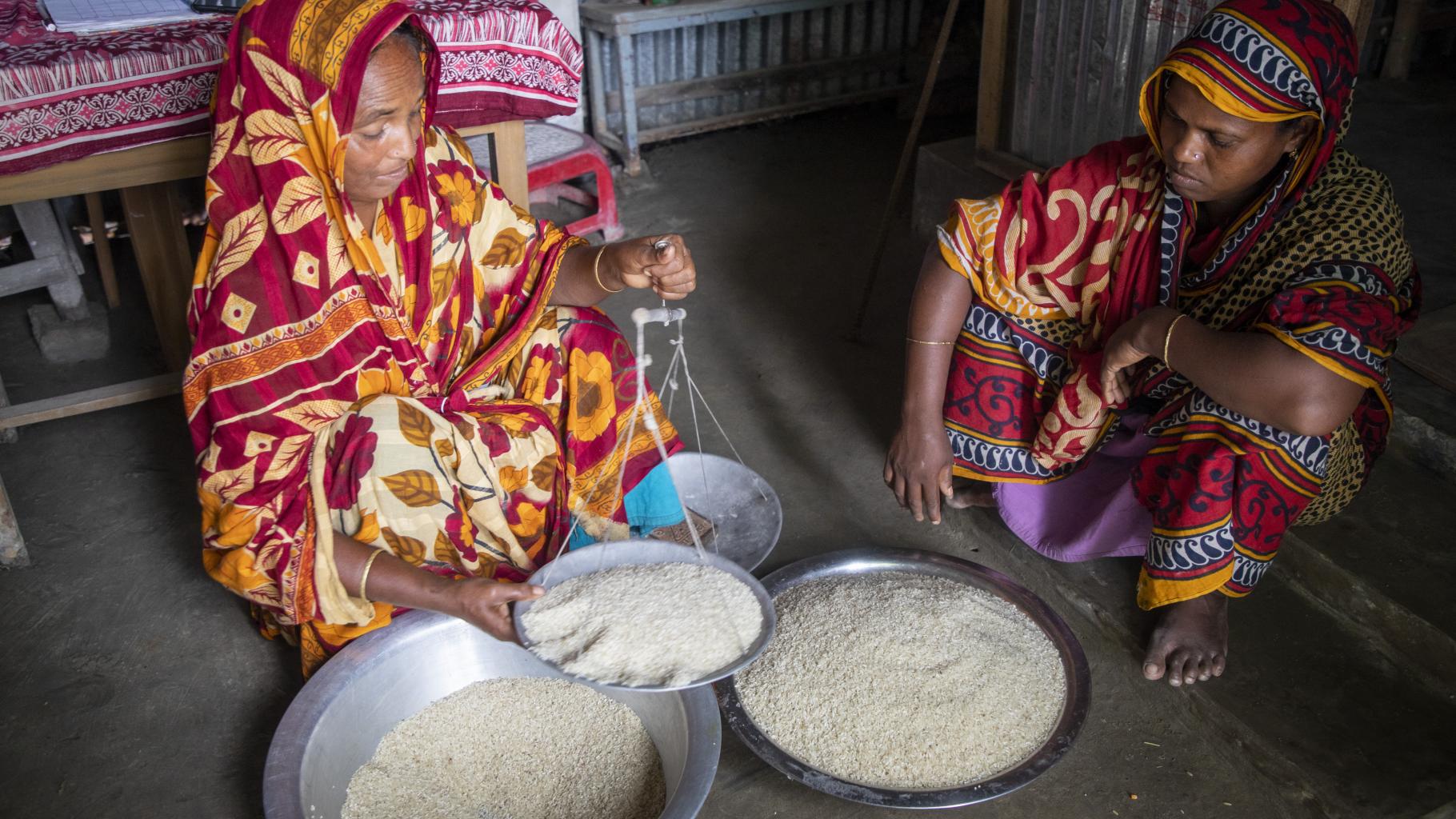 Eine Frau wiegt Reis mithilfe einer Schale, eine zweite Frau sitzt neben ihr