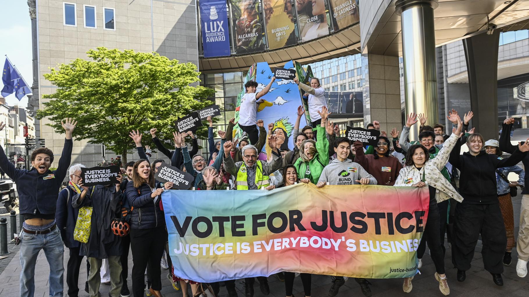 Eine Gruppe von etwa 30 Menschen hält vor dem Brüsseler Gebäude des EU-Parlaments ein Banner mit der Aufschrift „Vote for Justice – Justice is Everybody's Business“ und freut sich einen Keks.