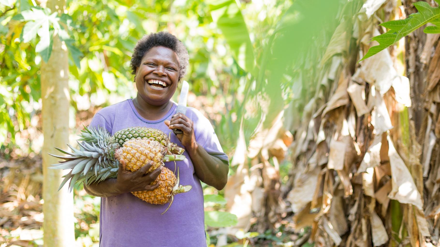 Eine lachende Frau mit Machete trägt Ananas