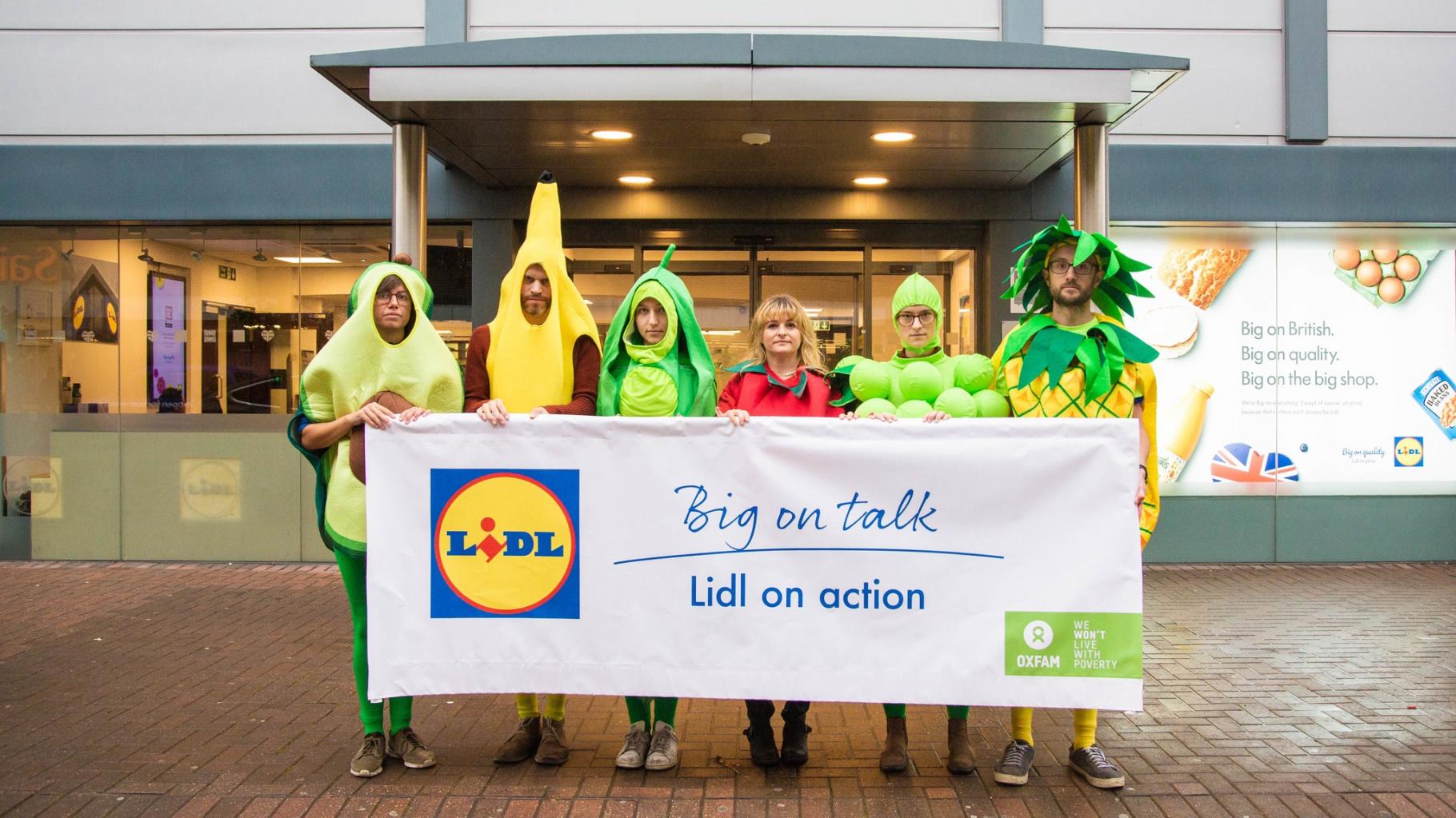 Als Früchte verkleidete Aktivist*innen halten ein Banner mit der Aufschrift: „Big on talk, Lidl on action“ vor der britischen Lidl-Zentrale