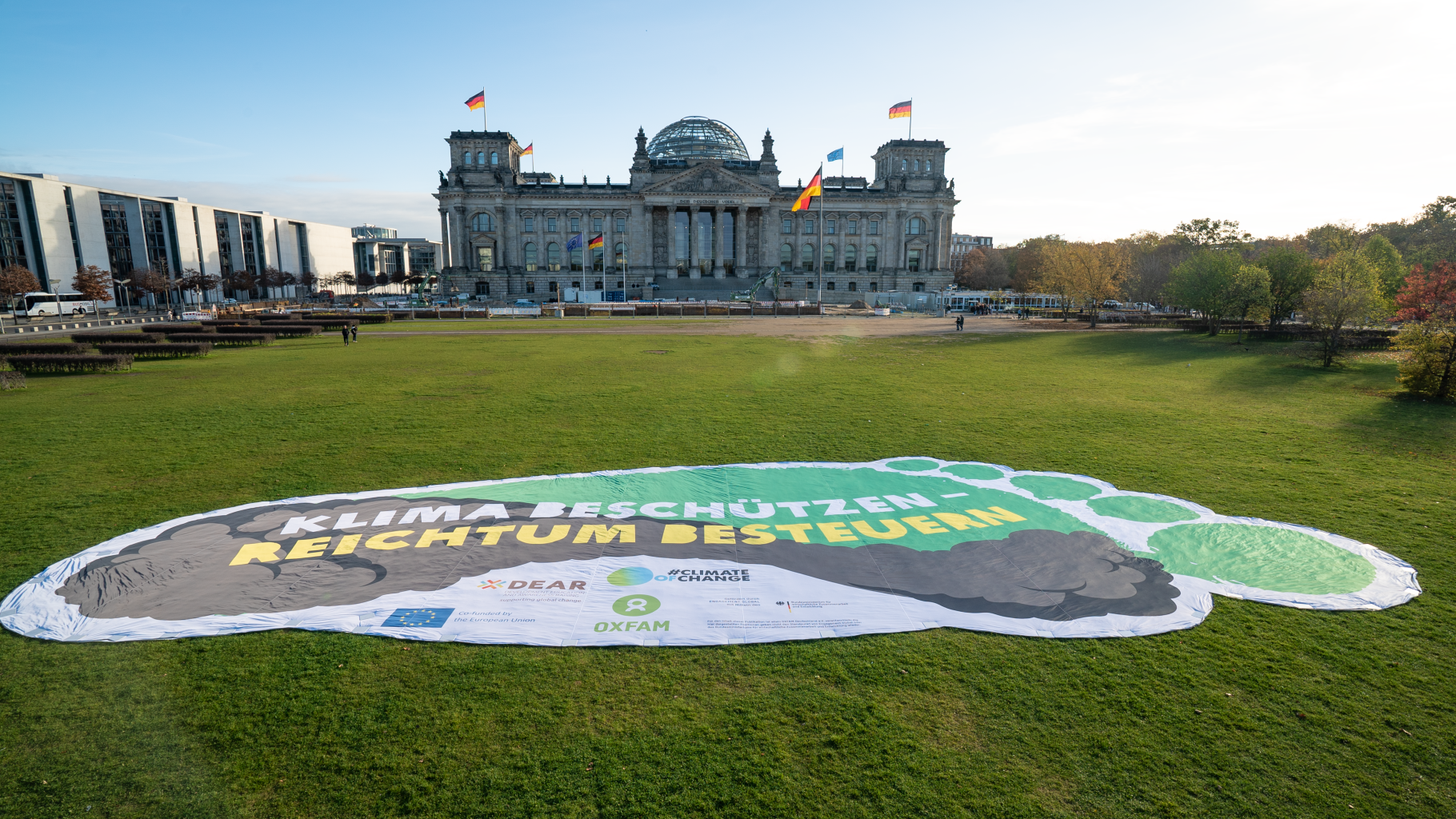 Überdemensionaler Fußabdruck als Tranparent auf der Wiese vor dem Reichstagsgebäude. Es trägt die Aufschrift "Klima beschützen - Reichtum bestuern"