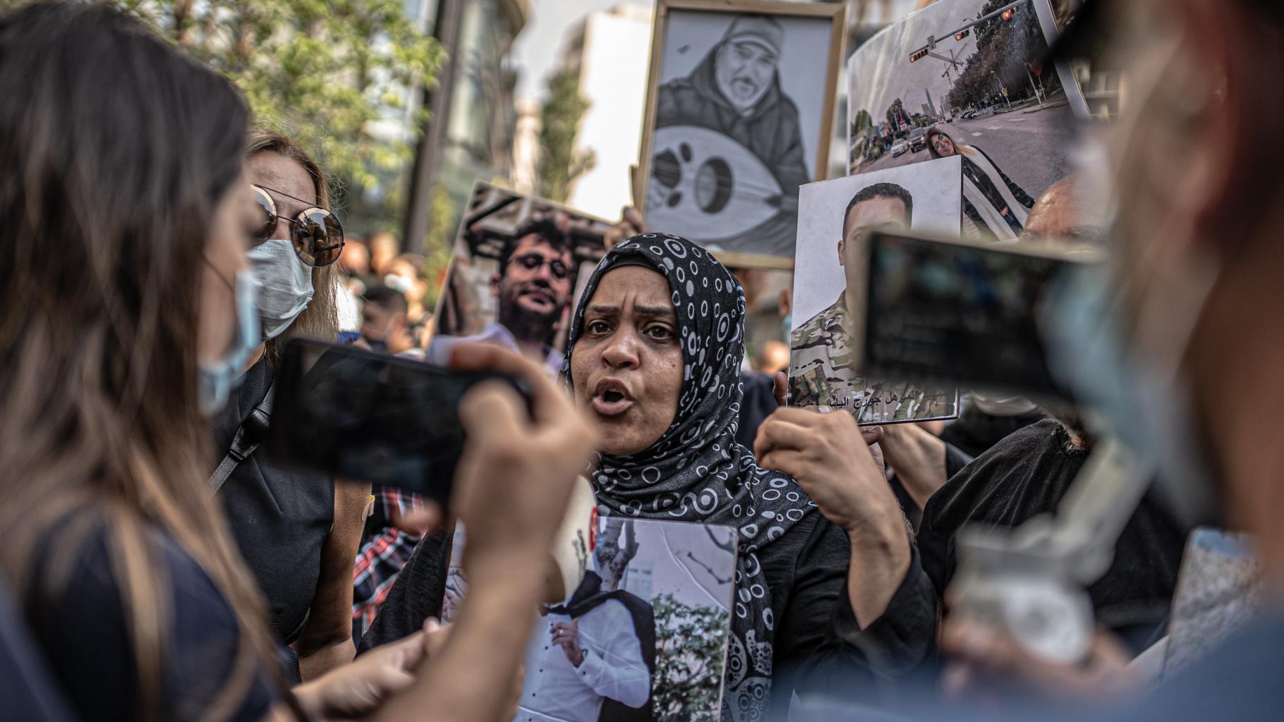 Rima Azzaher macht ein Statement inmitten einer Menschenmenge. Sie hält ein Foto ihres verstorbenen Bruders in den Händen.