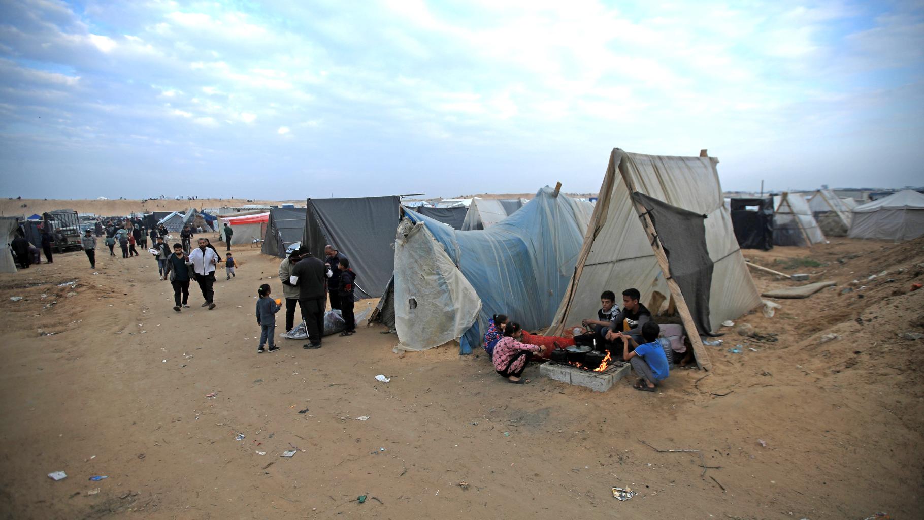 Eine Szene aus einem Camp in Rafah, Gaza. Kinder bereiten essen vor einem Zelt zu. Menschen teilen Wasser aus.