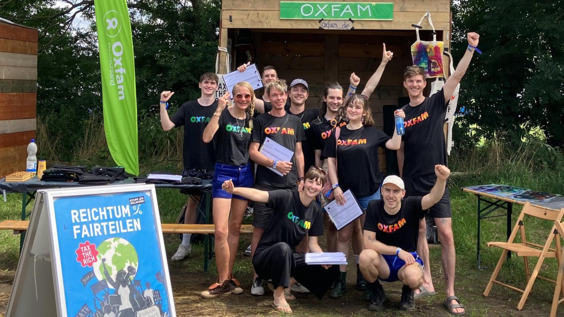 Eine Gruppe von Oxfam-Aktiven posiert mit Unterschriftenlisten vor dem Oxfam-Stand auf einem Festival